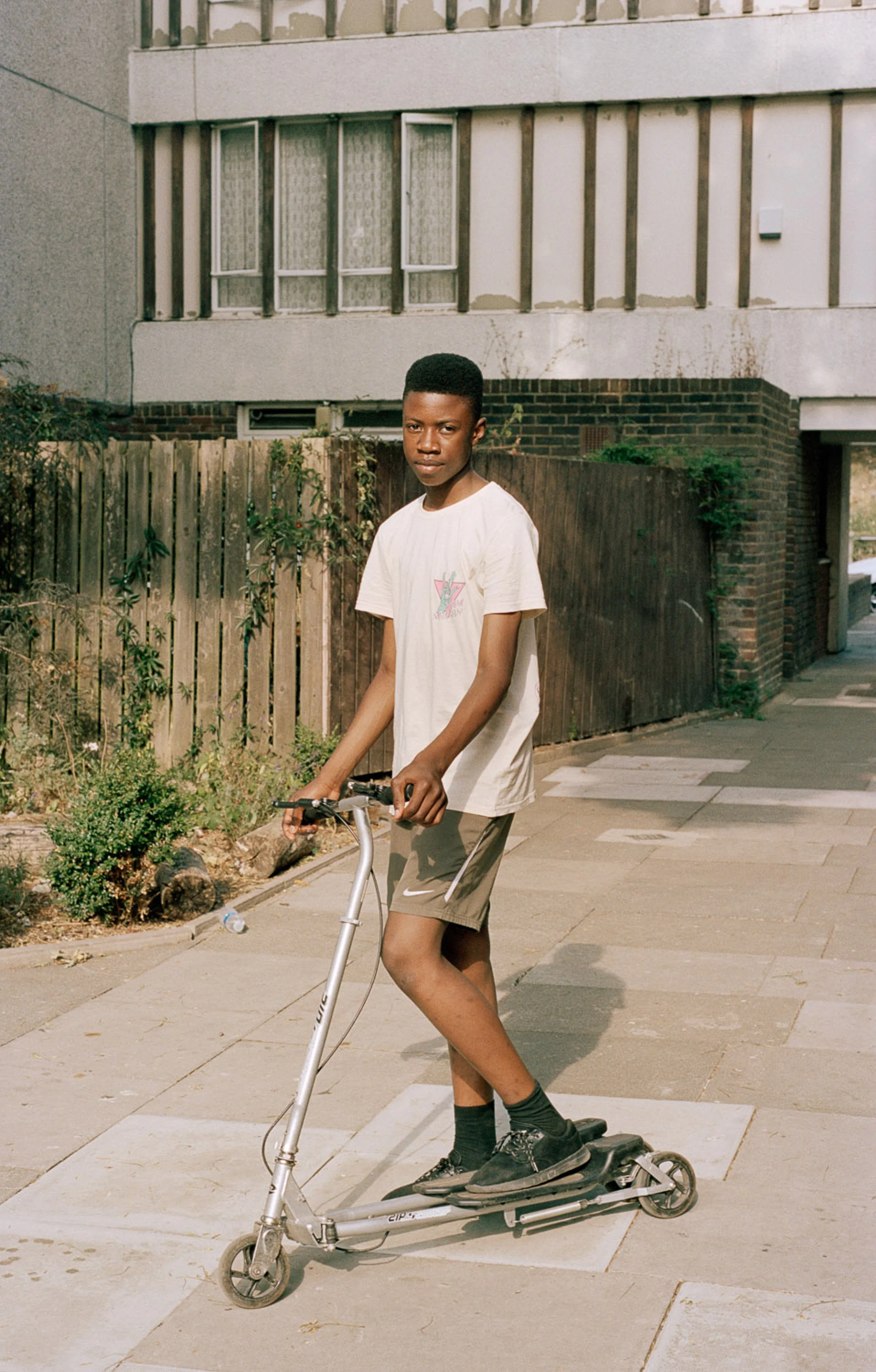 A young boy riding a silver scooter on a city sidewalk.
