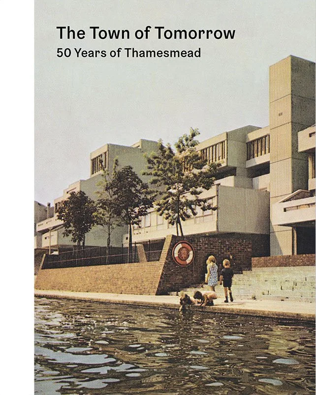 A waterfront scene featuring two children and two dogs by the water's edge, with modern architectural buildings and trees in the background, and a graphic circular emblem on the brick wall.