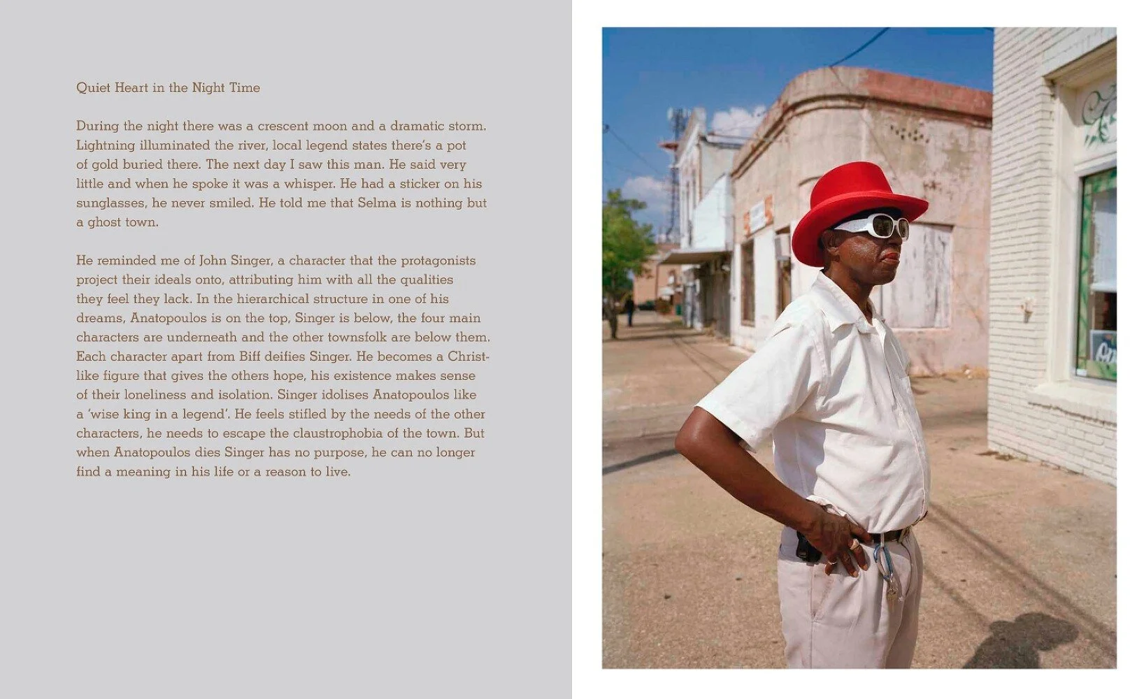 A man wearing a red hat, white shirt, and sunglasses stands on a sidewalk in a small town with old white and pink buildings in the background.