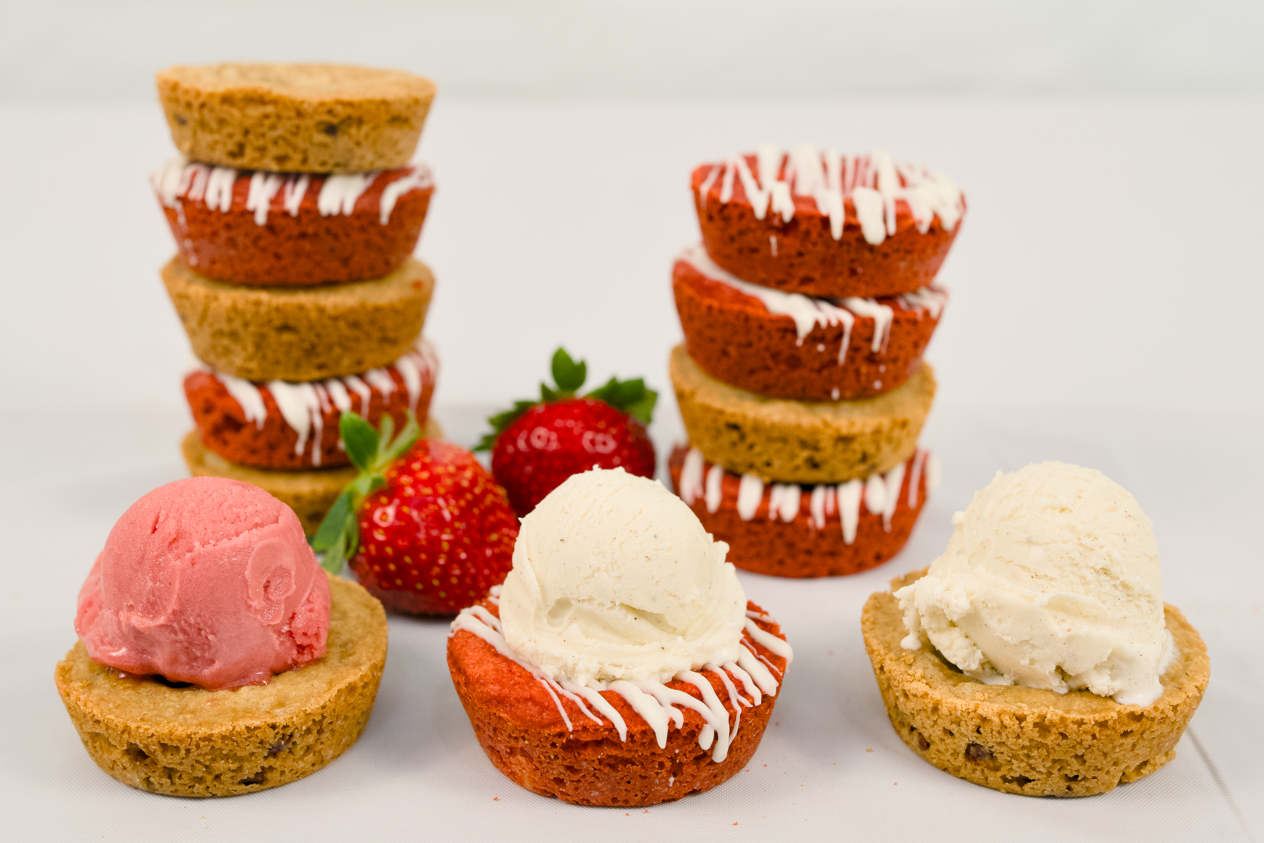 A display of strawberry shortcake desserts with vanilla and strawberry ice cream, fresh strawberries, and cookies, decorated with white icing.