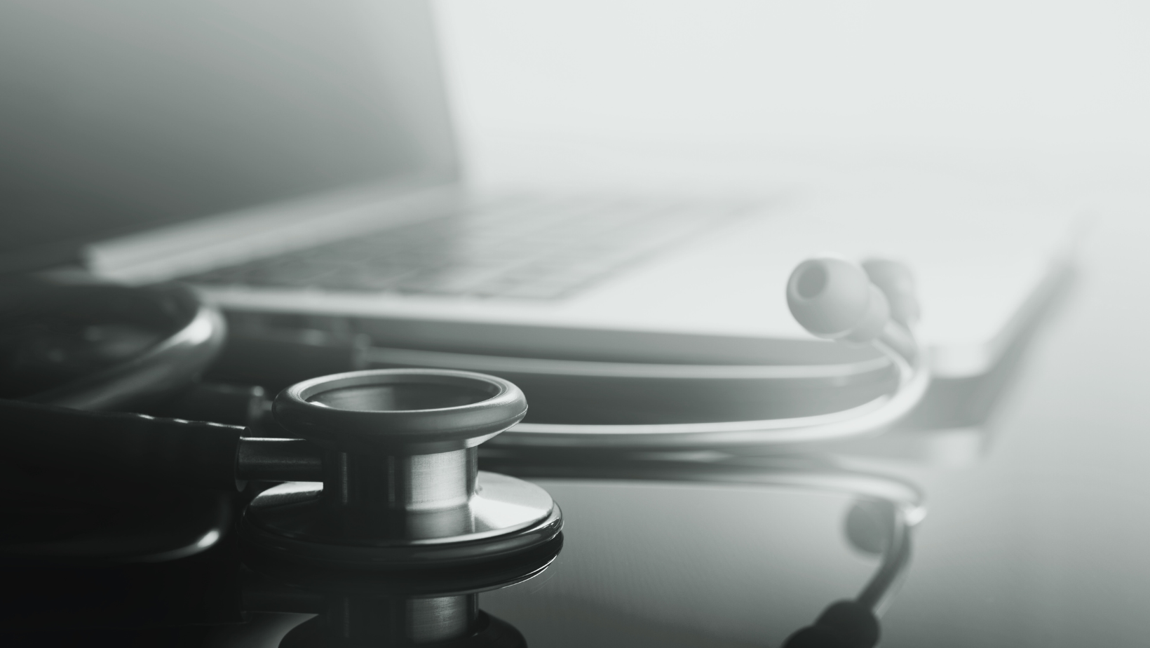 Stethoscope and laptop on a doctor’s desk in a clinical setting.