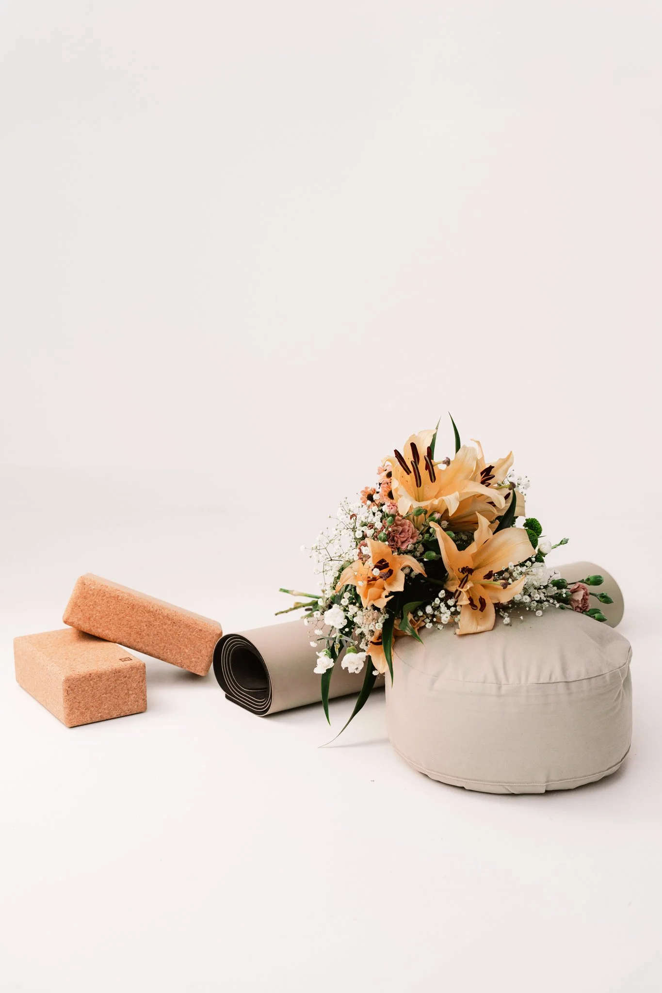 Blumenstrauß, Yogakissen, Yogamatte, zwei Yogablöcke, auf neutralem Hintergrund.