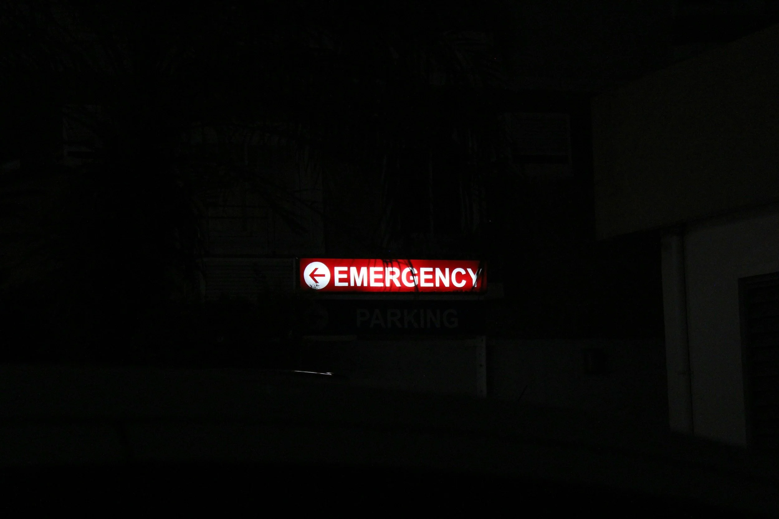 Illuminated red and white emergency sign with a left arrow and the word 'EMERGENCY' at night.
