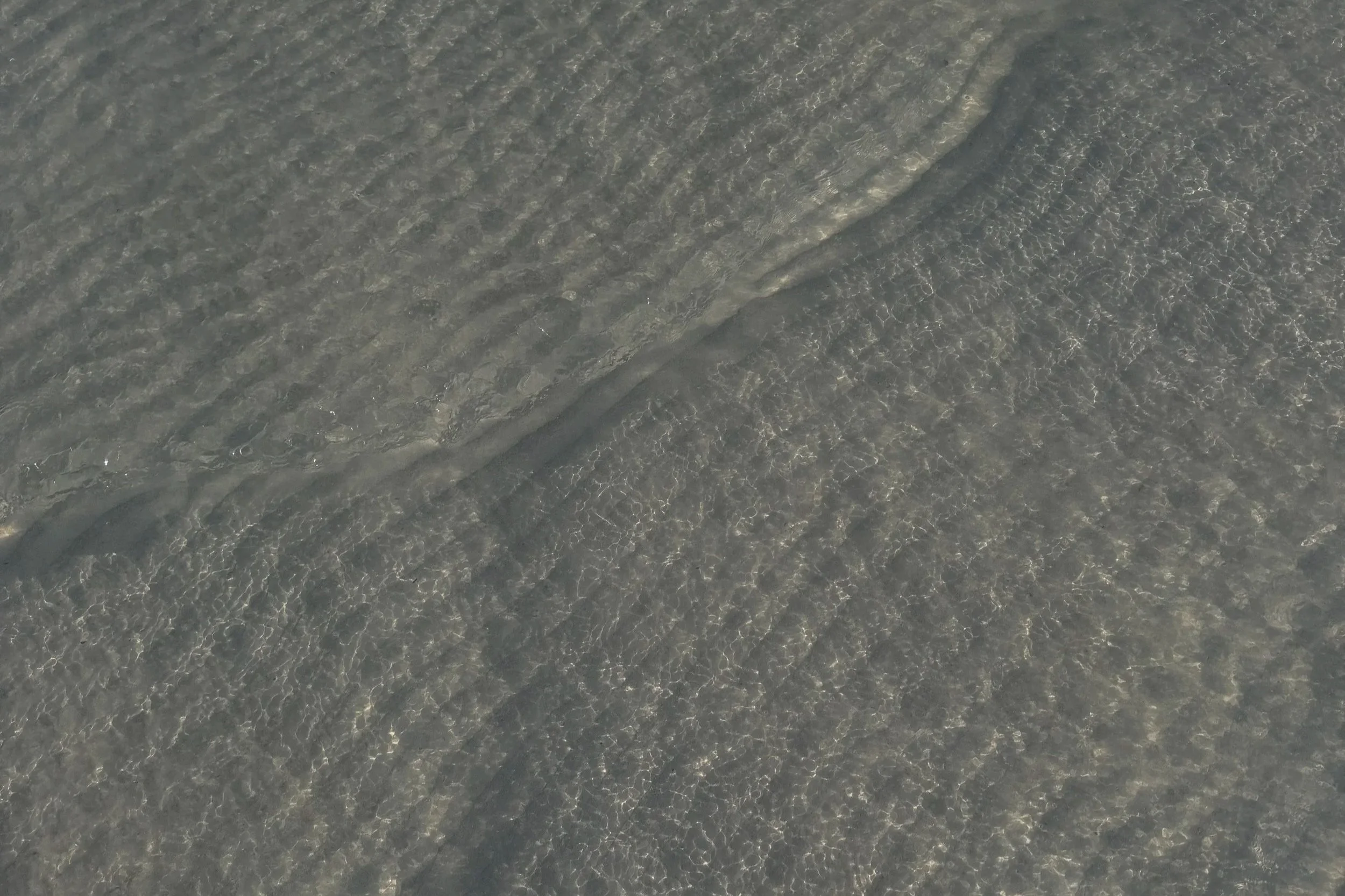 Close-up aerial view of clear ocean water with gentle waves and sunlight reflections.