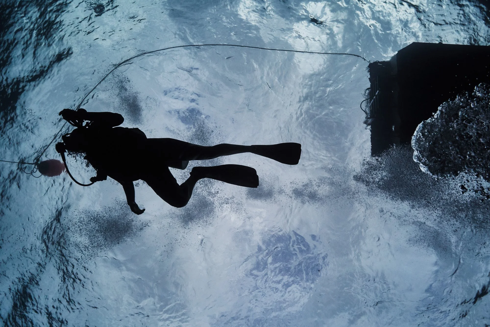 Silhouette of a person in scuba gear jumping into water from a boat, with splashes and ripples in the water, in Cayman Islands.