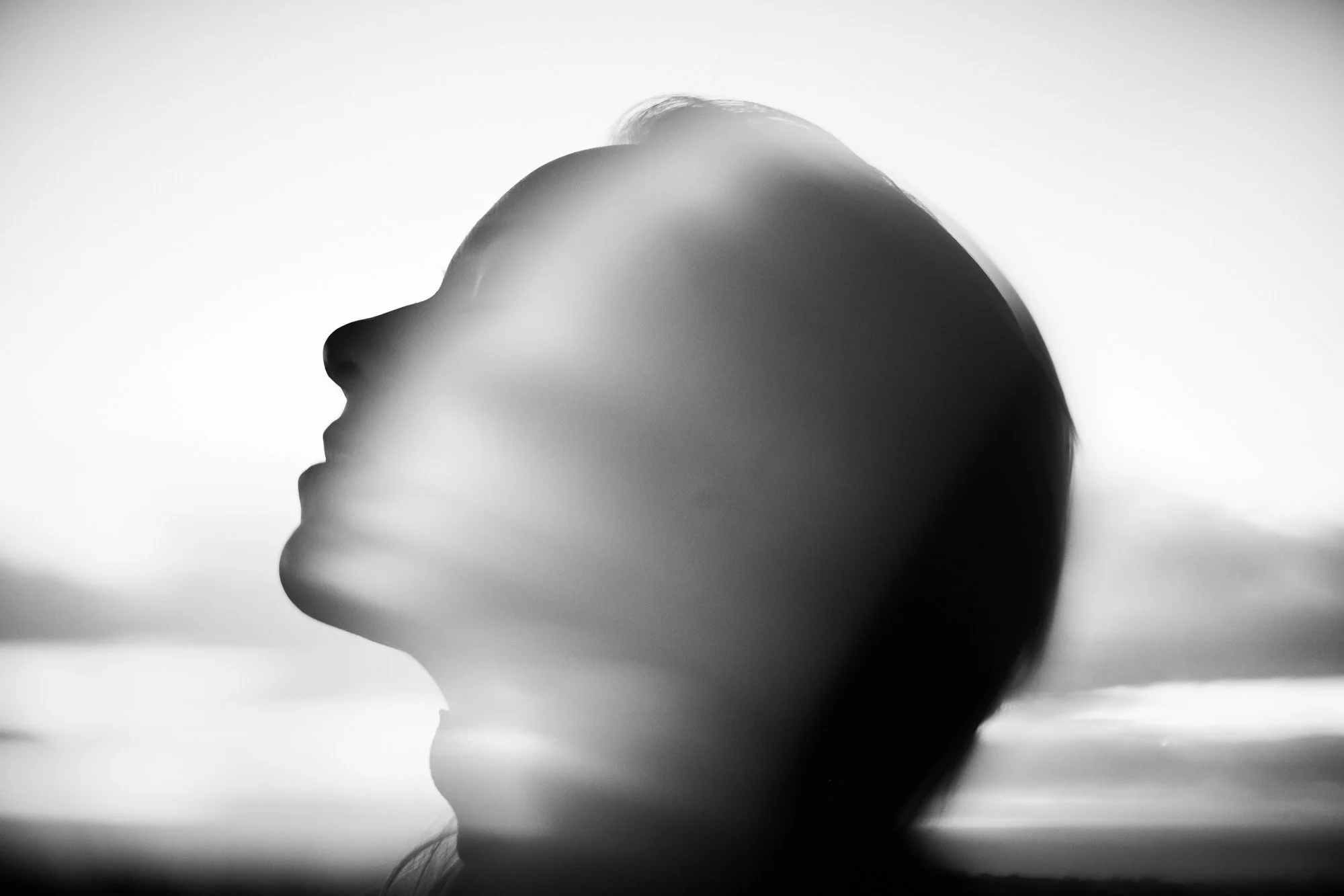 Black and white artistic photo of Sami Freeman's profile with her eyes closed, head tilted slightly upward, against a blurred background.