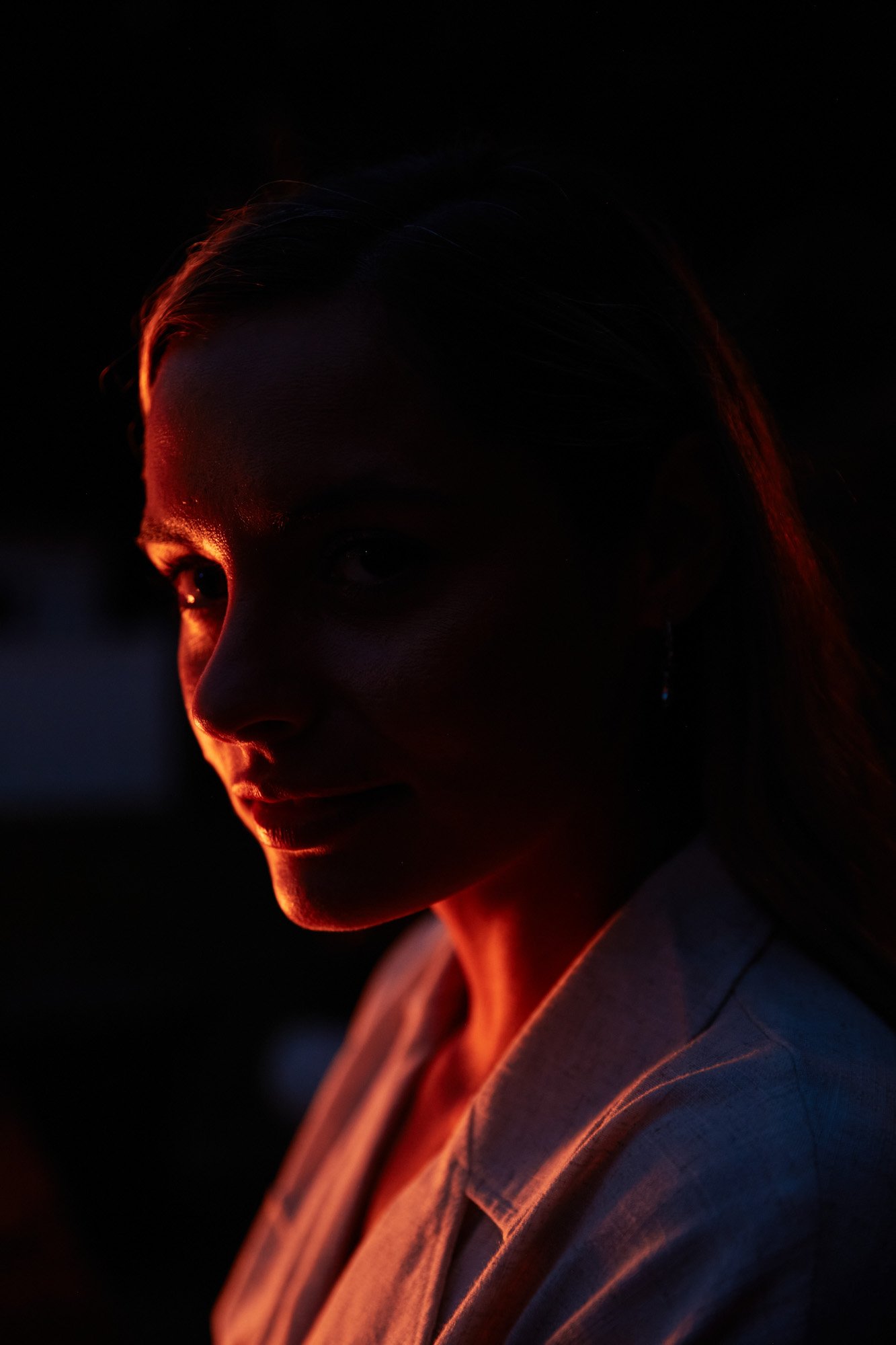 A woman with her face partially illuminated by warm, orange fire light, creating a silhouette with shadows in a dark background.