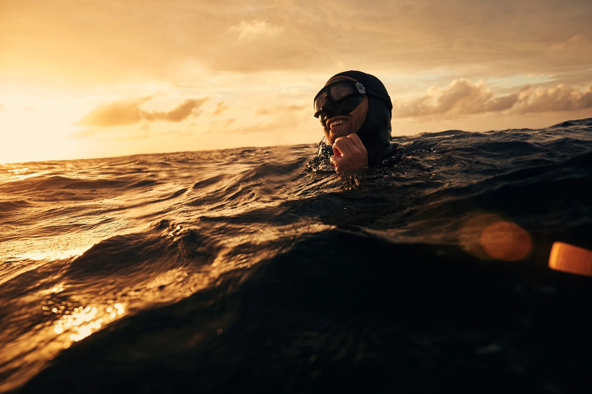 A man in a wetsuit and freediving gear swimming in the ocean during sunset in Roatan Honduras, smiling and enjoying the moment.