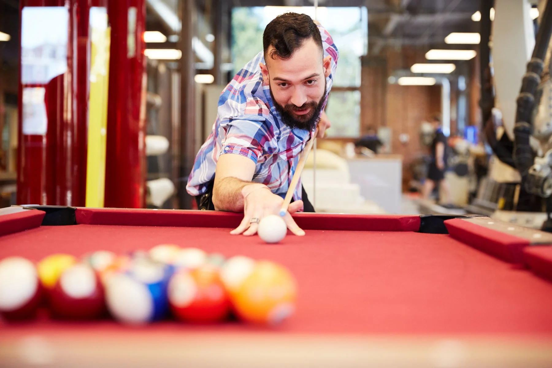 Man playing pool, focusing on a shot with a red billiards table in a modern indoor setting at Piaggio Fast Forward in Boston Massachusetts