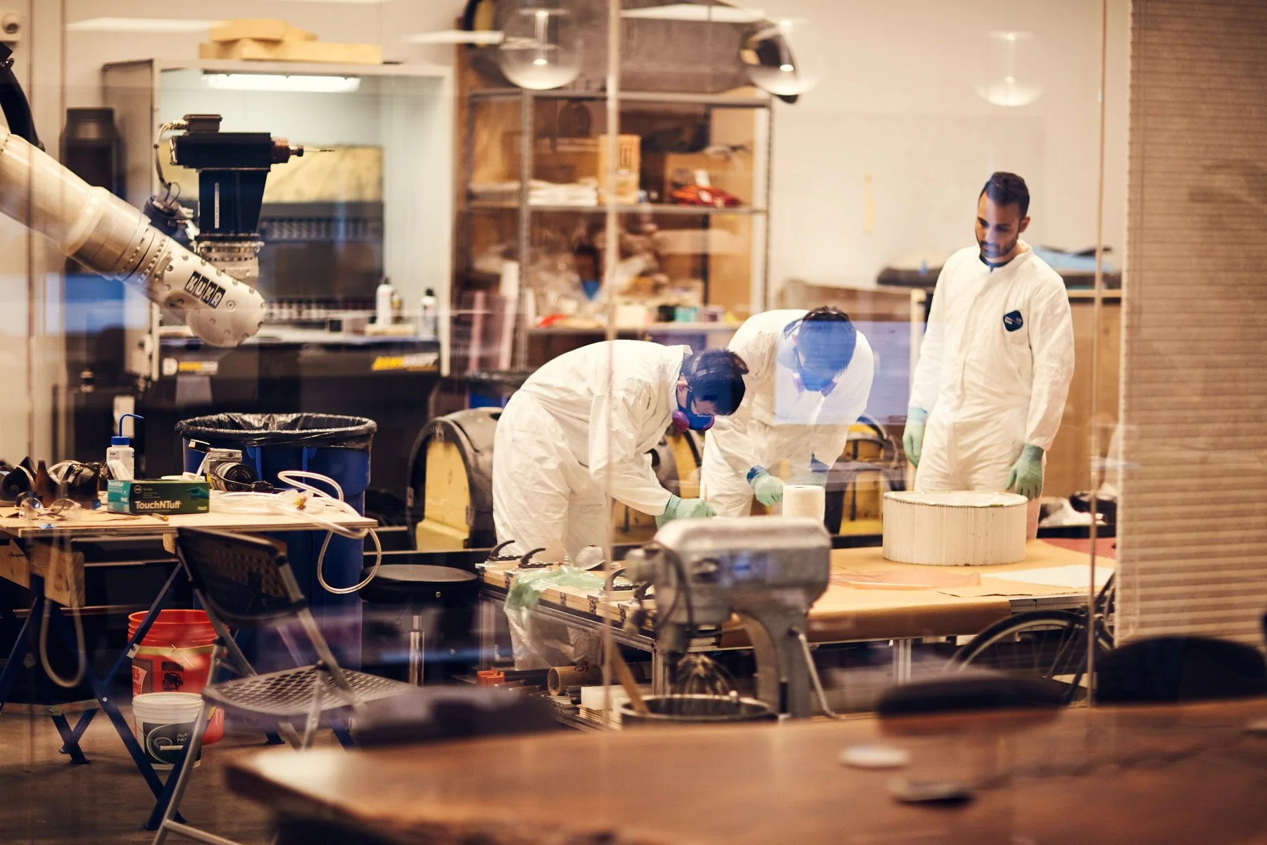 Laboratory with three people in protective suits working, surrounded by equipment and a robotic arm at Piaggio Fast Forward in Boston Massachusetts