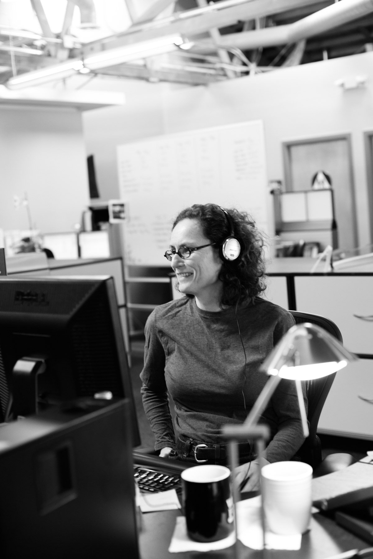 Black and white photo of a person wearing headphones, smiling at a computer in an office Wingman Advertising in Los Angeles California