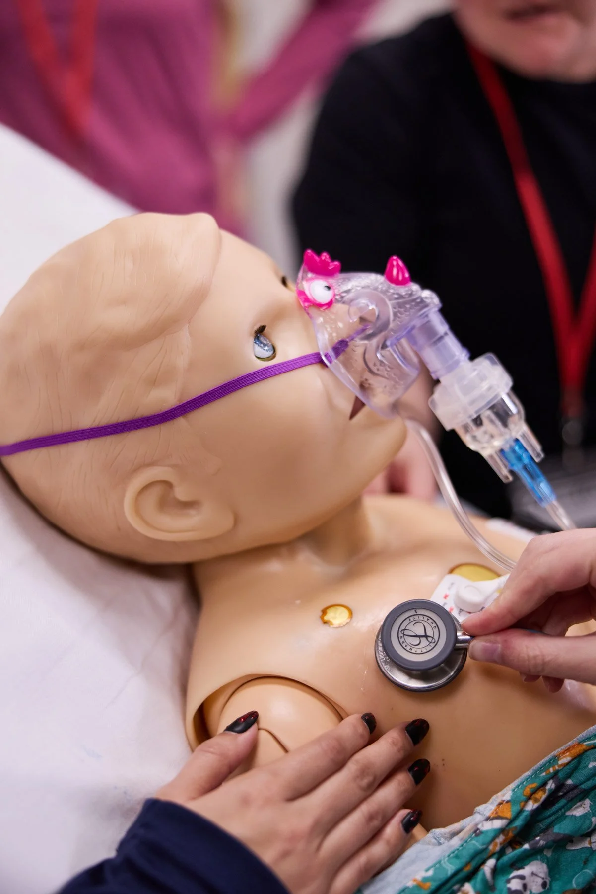 A medical training mannequin of a child with a stethoscope on its chest and a respiratory mask attached, simulating a healthcare scenario at Cornell PEM Base Camp