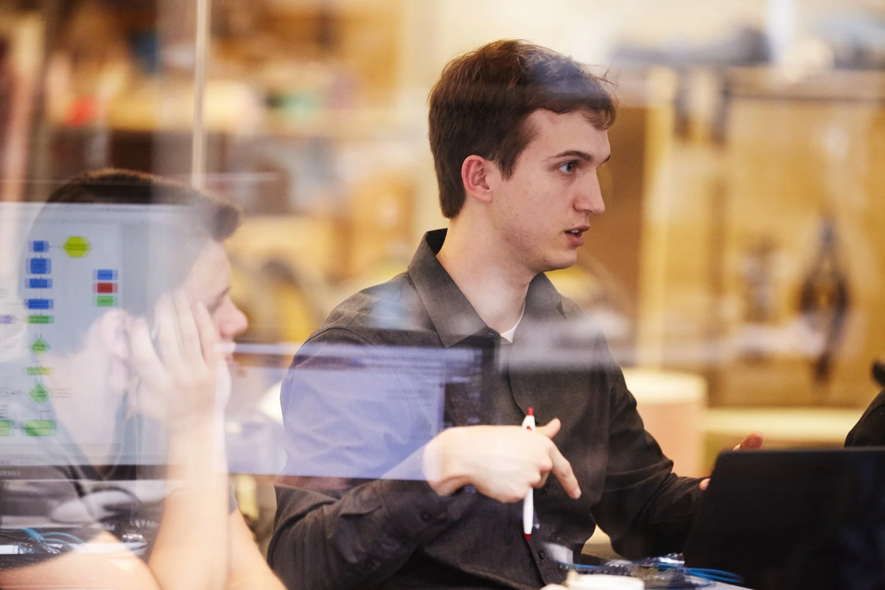 Two colleagues in a meeting room discussing work, one holding a pen. A computer screen with charts is visible in the foreground at Piaggio Fast Forward in Boston Massachusetts