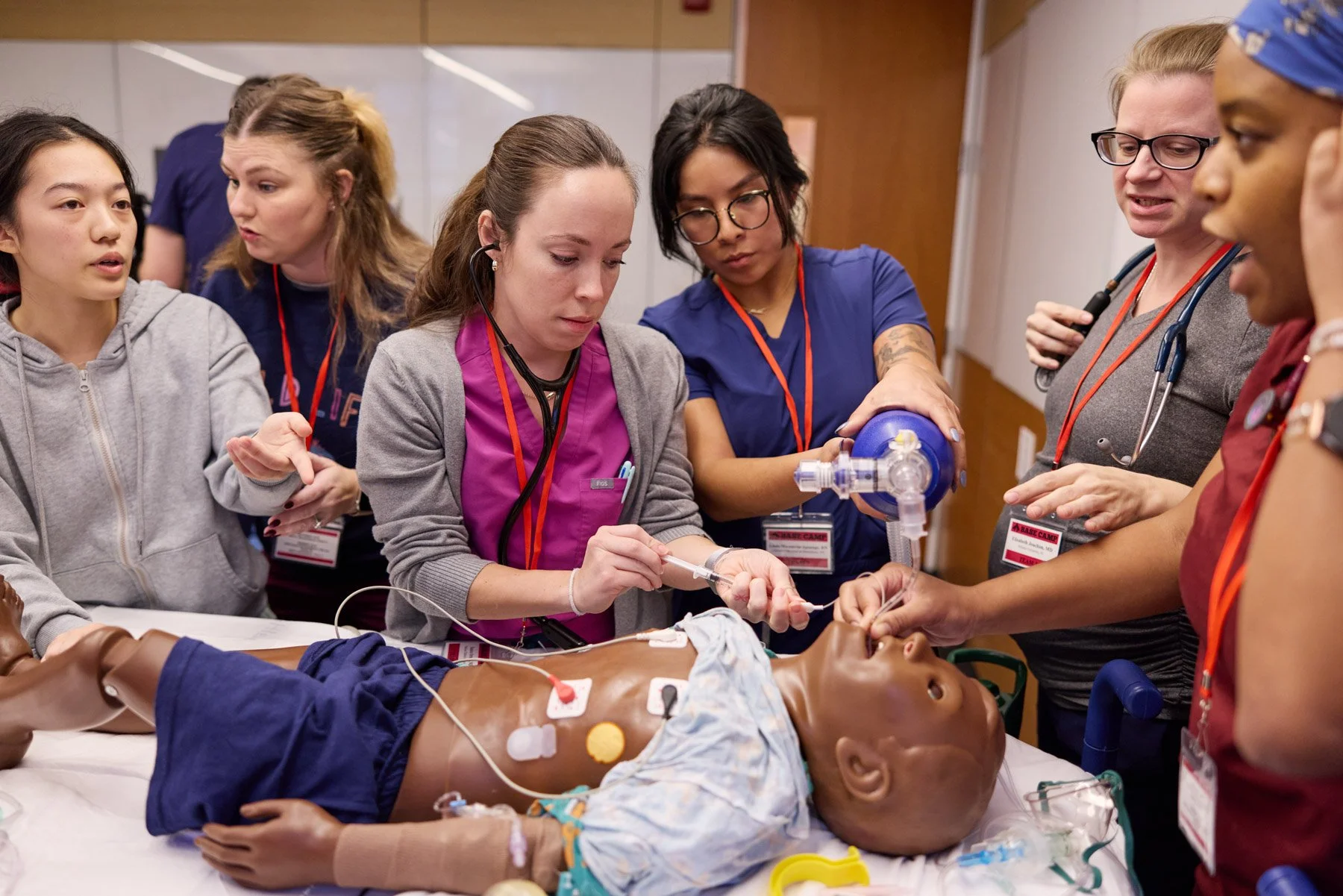 Medical students practicing emergency procedures on a pediatric manikin with medical equipment and stethoscopes at Cornell PEM Base Camp