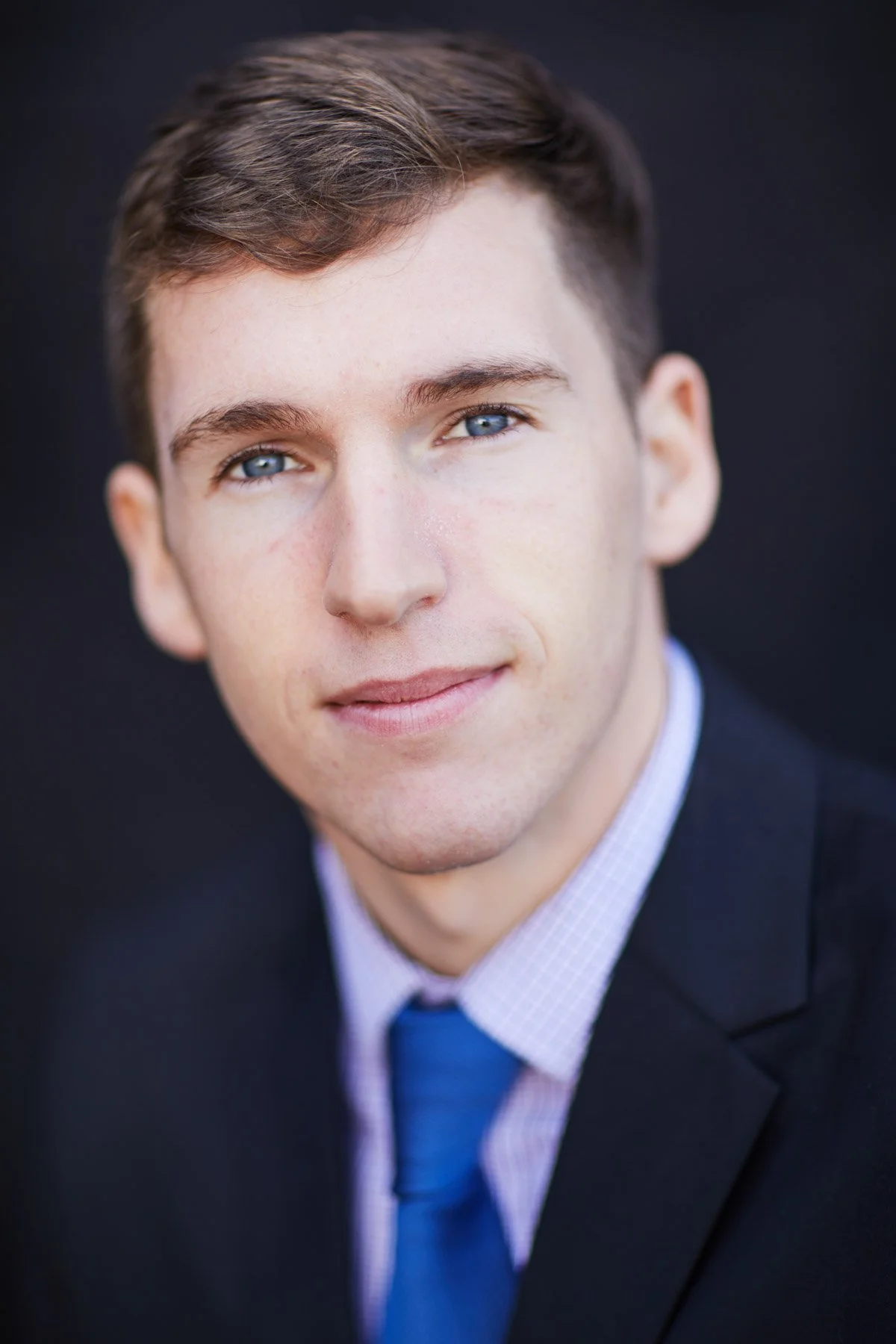 Portrait of a man in a suit and blue tie, staring directly at the camera, against a dark background.