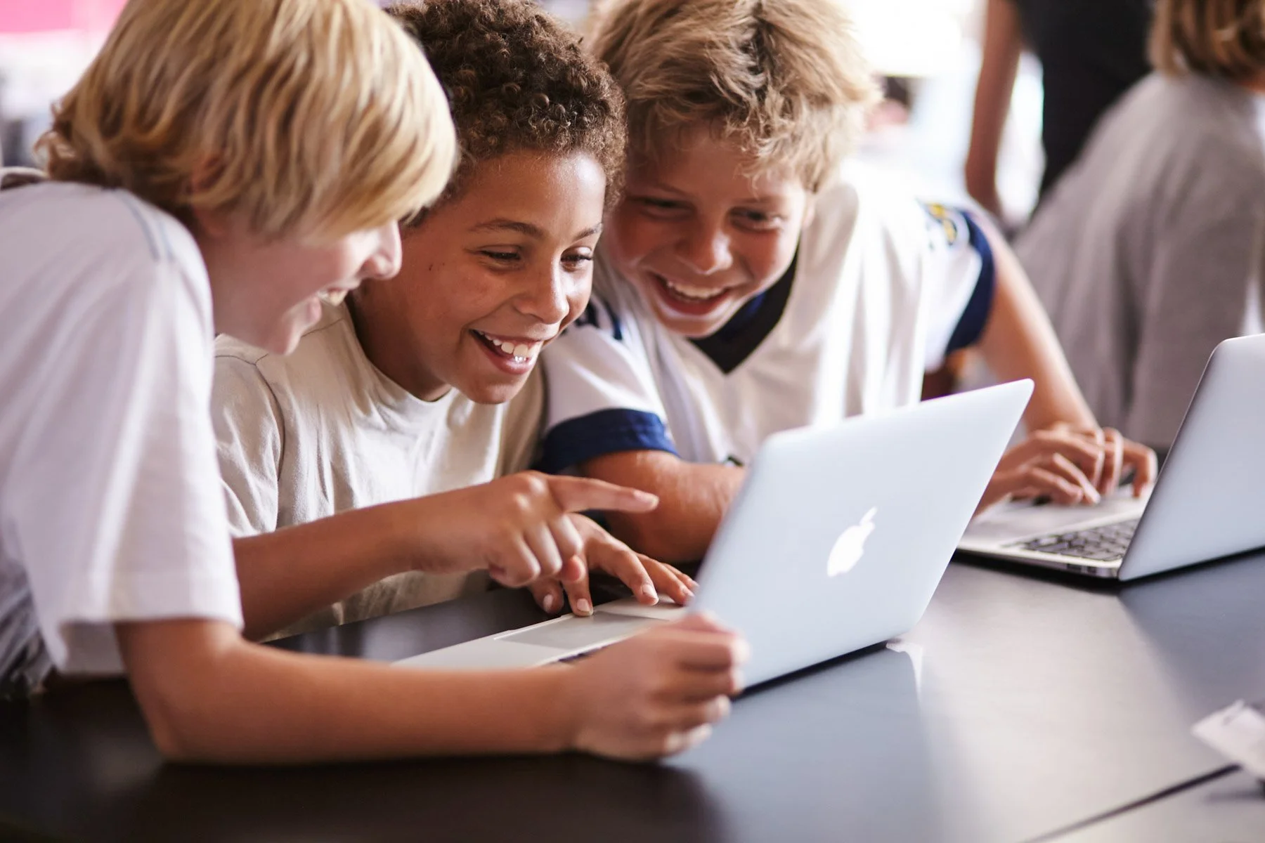Three young students smiling and looking at a laptop together.