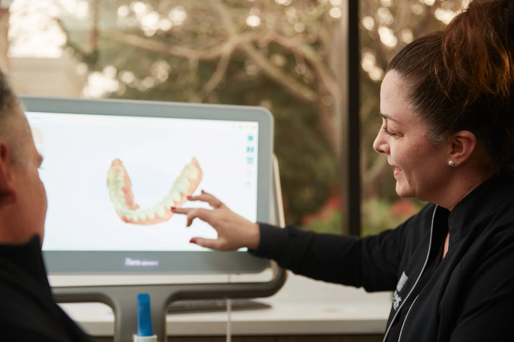 Dental professional showing patient 3D teeth model on a screen.