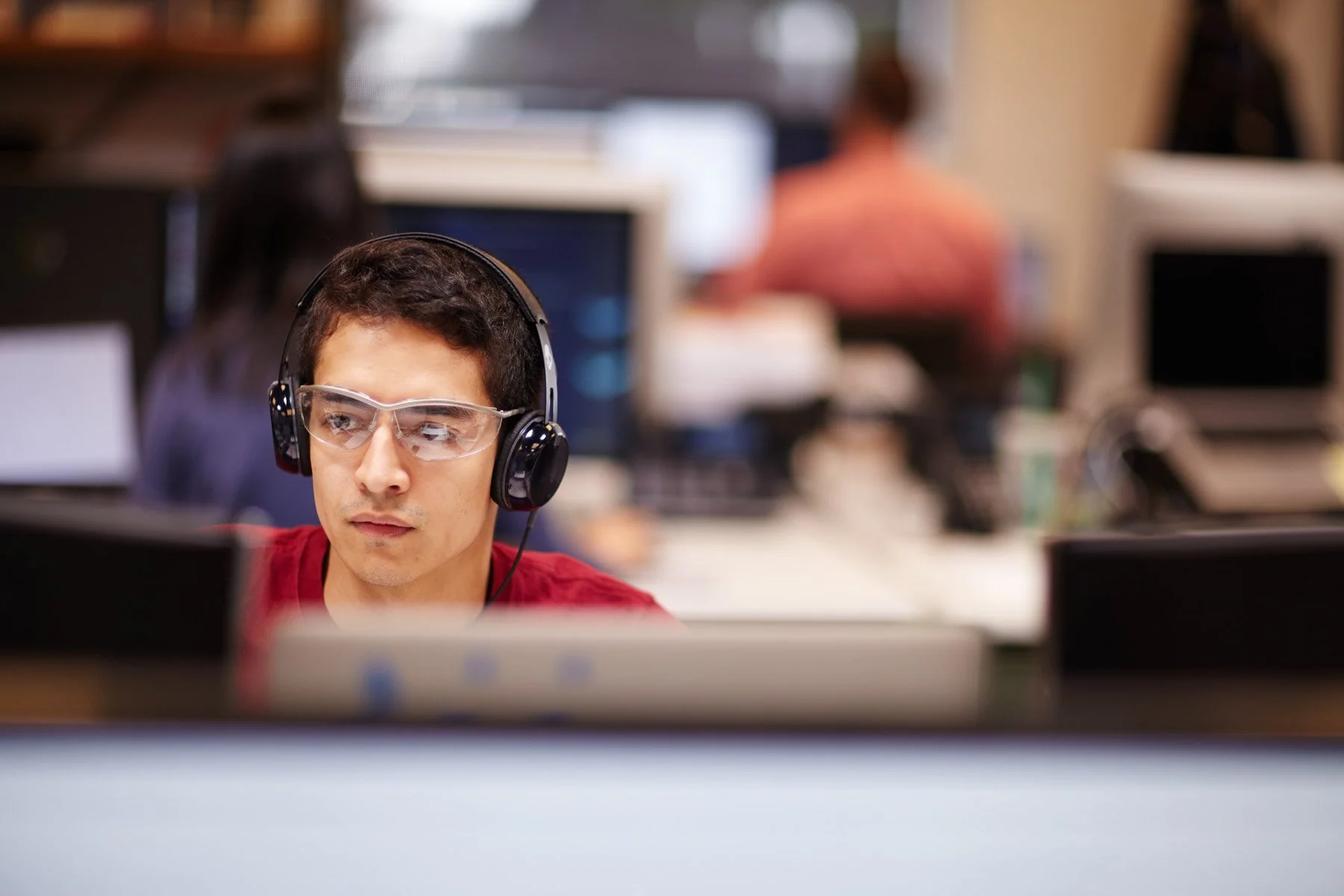 Young man wearing headphones and safety glasses working with computers in a modern office for Piaggio Fast Forward in Boston Massachusetts