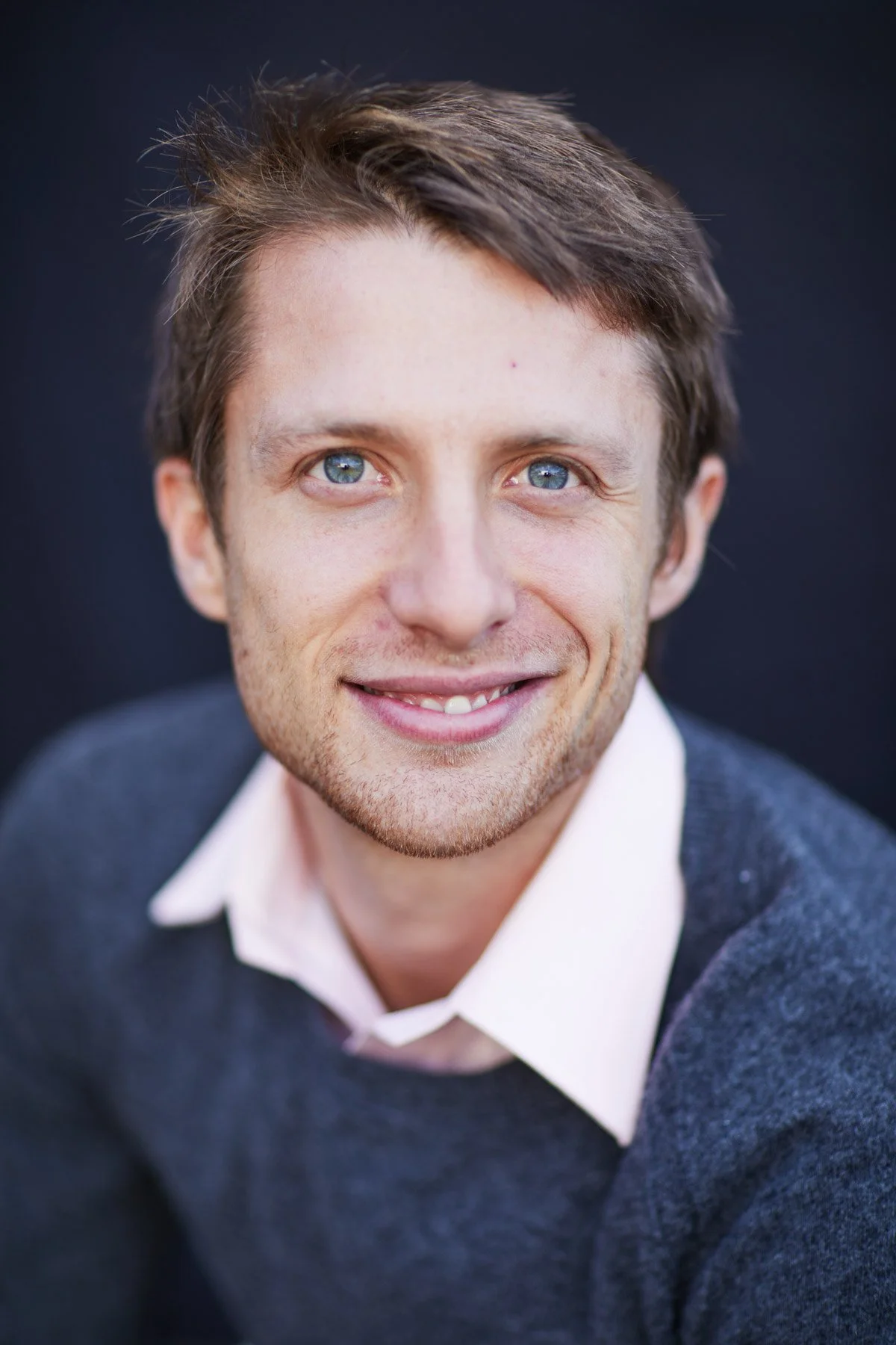 Man smiling with short brown hair, wearing a gray sweater and white collared shirt for Piaggio Fast Forward in Boston Massachusetts