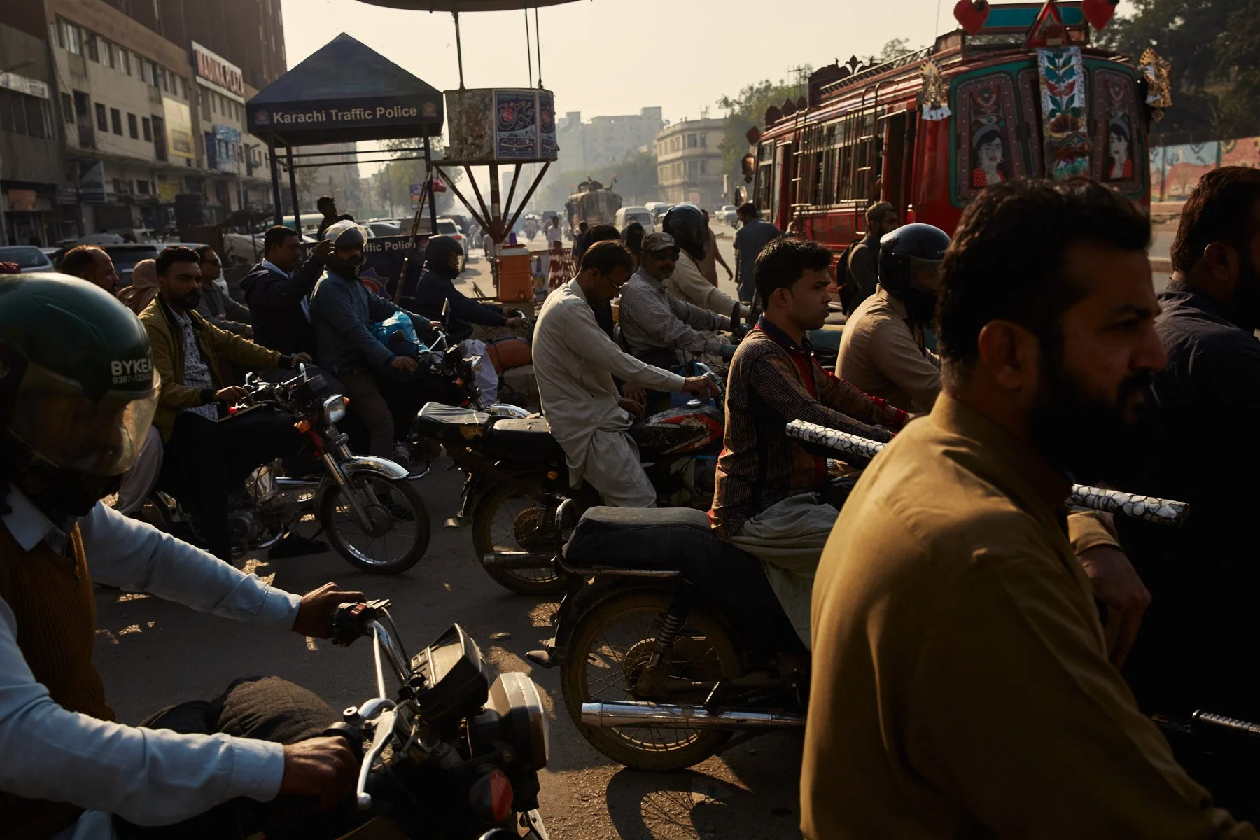 Traffic scene on MA Jinnah Road in Karachi Pakistan with motorcycles, a red decorative bus, and a Karachi Traffic Police booth on a busy street.