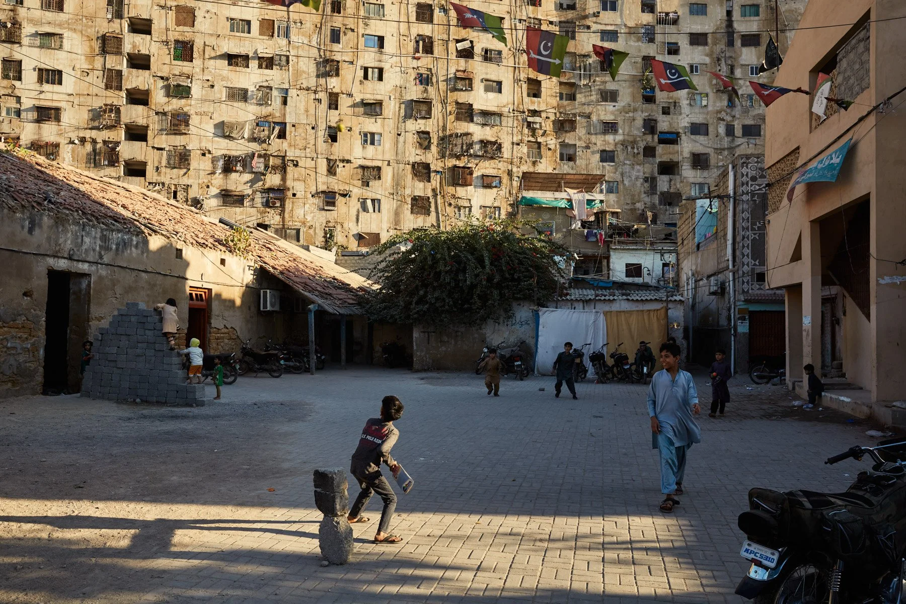 Children playing and walking in a courtyard surrounded by old and weathered buildings with laundry hanging from above in an urban area of Karachi Pakistan.