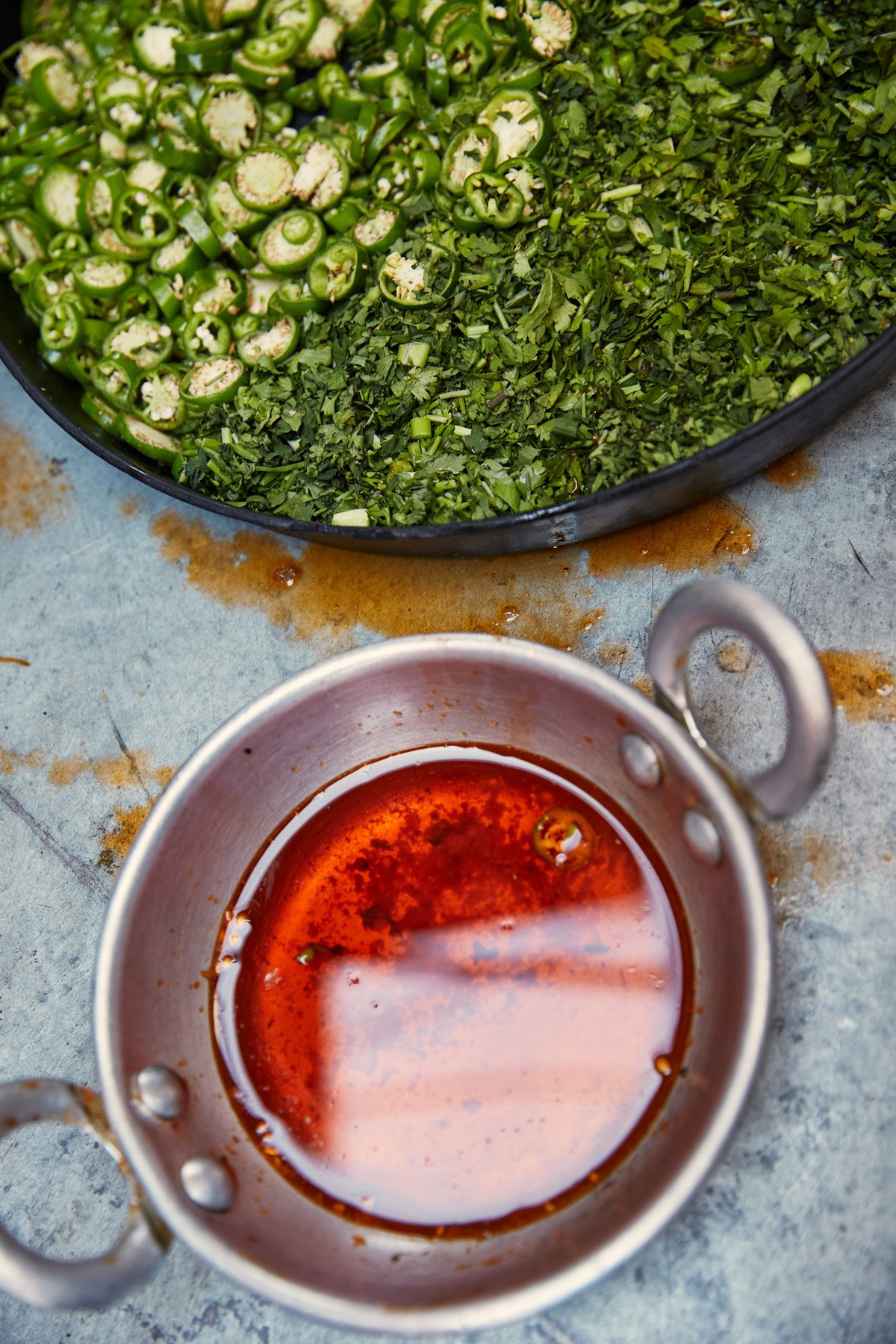 Chopped fresh herbs and sliced jalapeños on a black tray with a small pot of hot sauce nearby on a gray surface. Karachi Pakistan