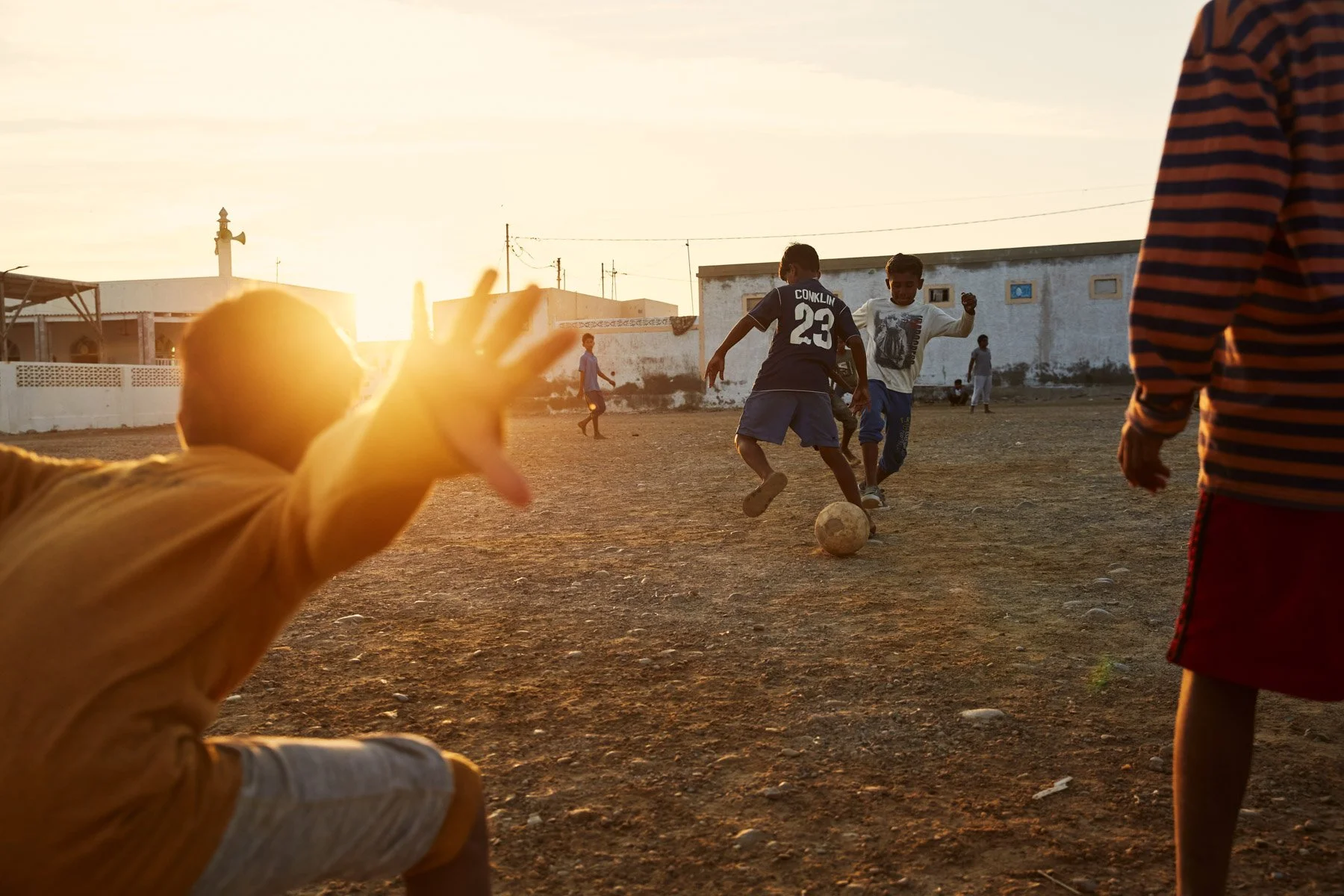 Children playing soccer on a dirt field during sunset in French Beach Karachi Pakistan