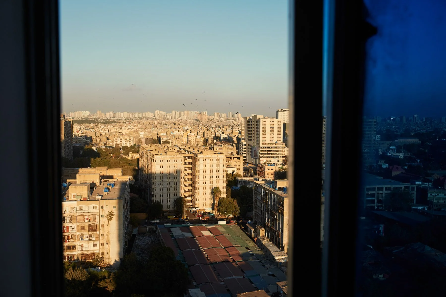 Cityscape view of Karachi Pakistan. Numerous buildings, some sunlight, some in shade, seen through a window at sunset.