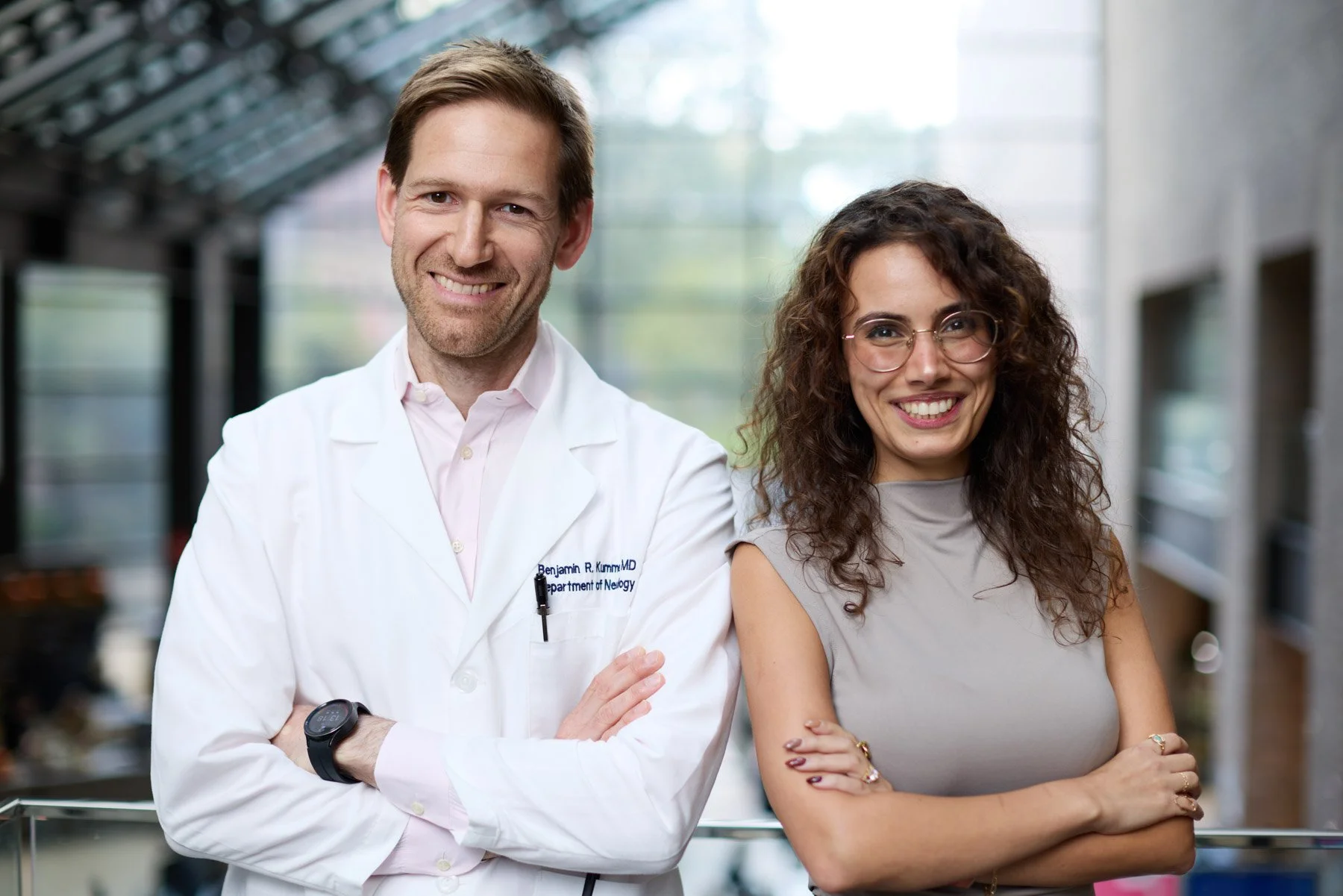Doctor Ben Kummer and a researcher Asala Erekat standing together in the atrium of Mount Sinai, both smiling with arms crossed. At Mount Sinai Hospital in New York City