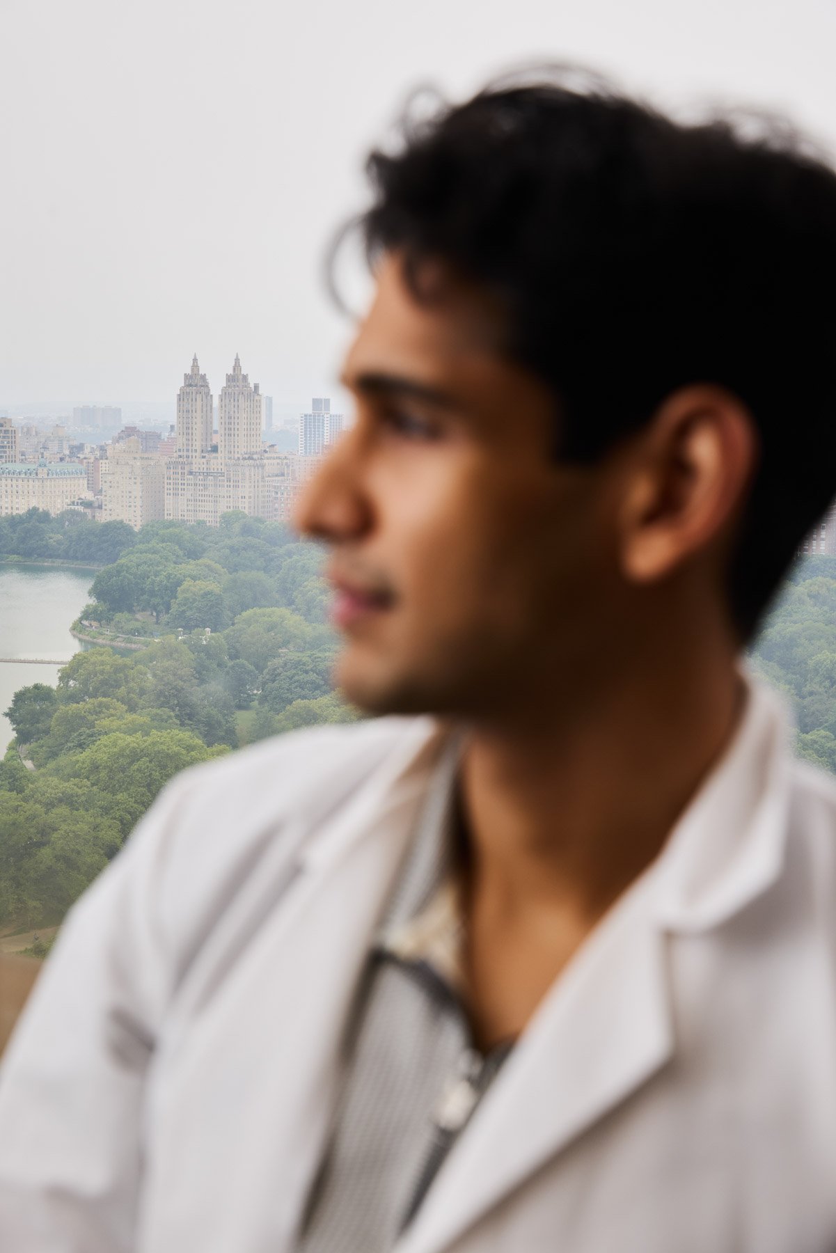 A scientist Ayman Mohammad wearing a white lab coat, blurry in the foreground with Central Park in the background. At Mount Sinai hospital in New York City. 