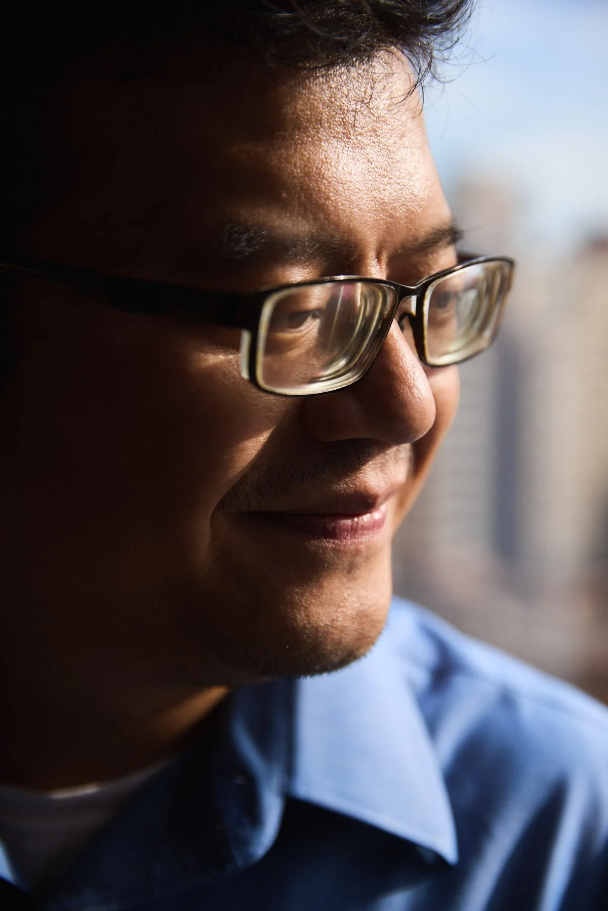 A researcher Doctor Xiaotao Zhang wearing glasses smiling while looking out a window during daytime. At Mount Sinai Hospital in New York City