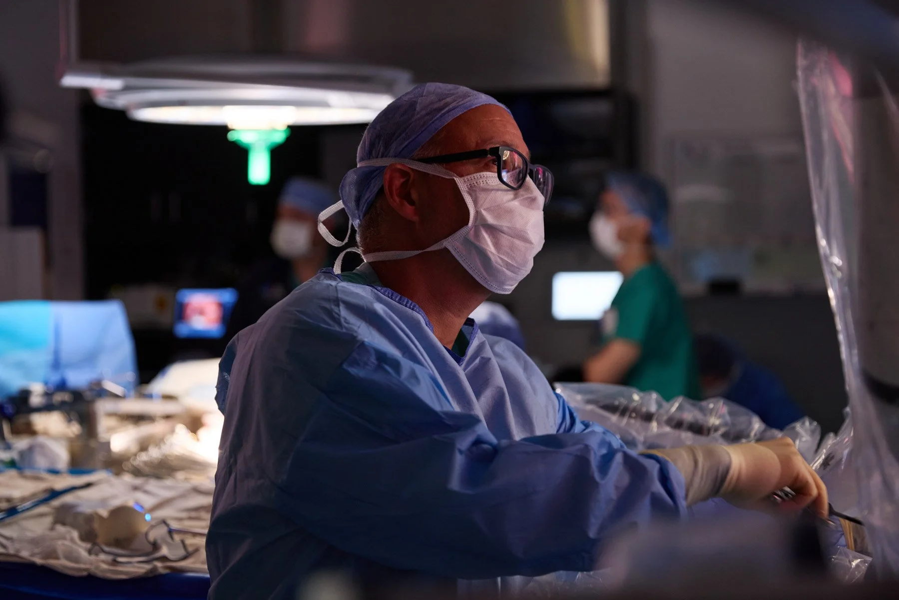 A surgical team led by Dr Andrew Kaufman in scrubs, masks, and protective eyewear working in an operating room with medical equipment and monitors visible in the background. At Mount Sinai Hospital in New York City
