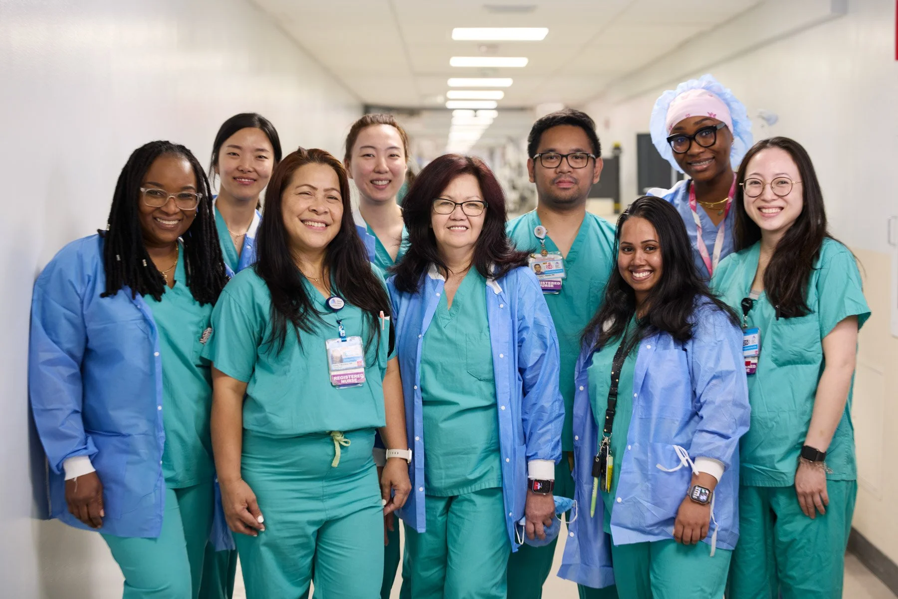Group of healthcare professionals in scrubs and lab coats smiling in a hospital corridor at Mount Sinai hospital in New York City
