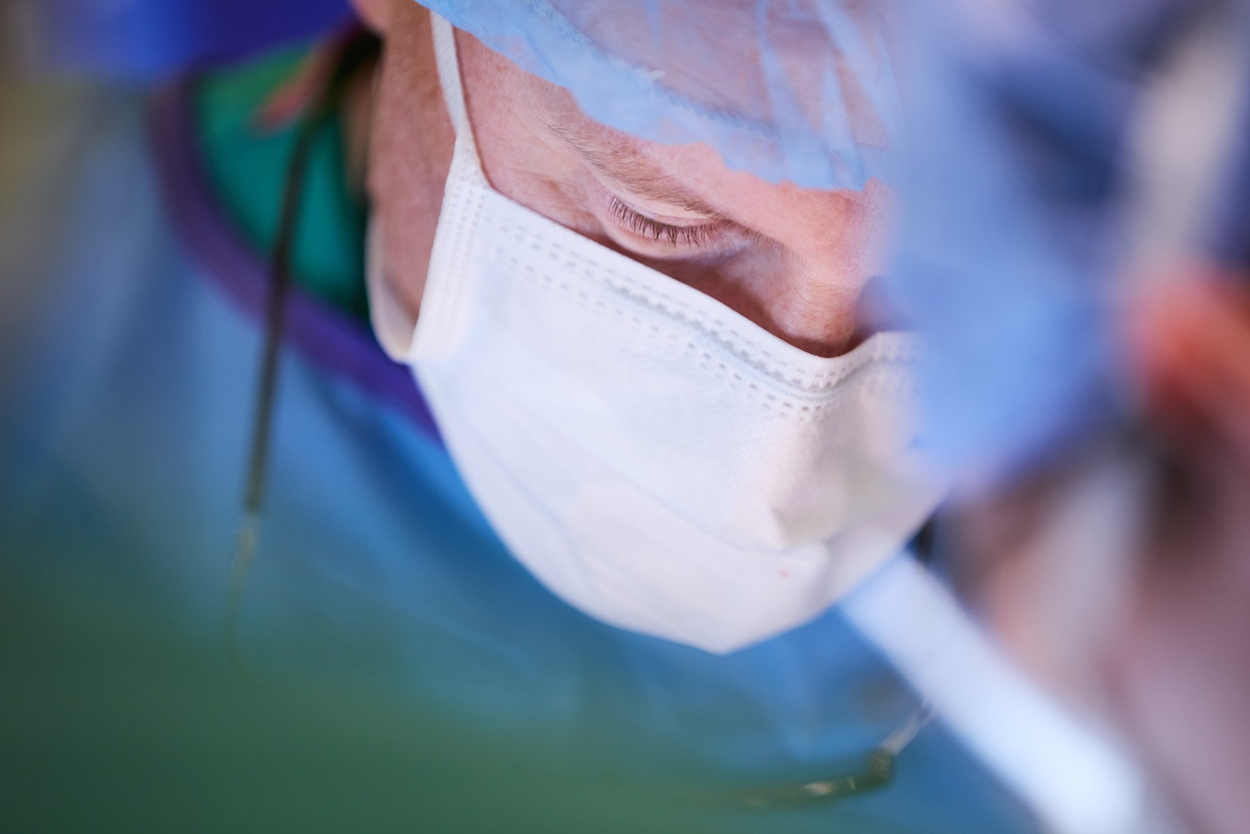 Close-up of a male surgeon wearing a white face mask and colorful surgical cap, focusing intently on their task. At Mount Sinai hospital in New York City