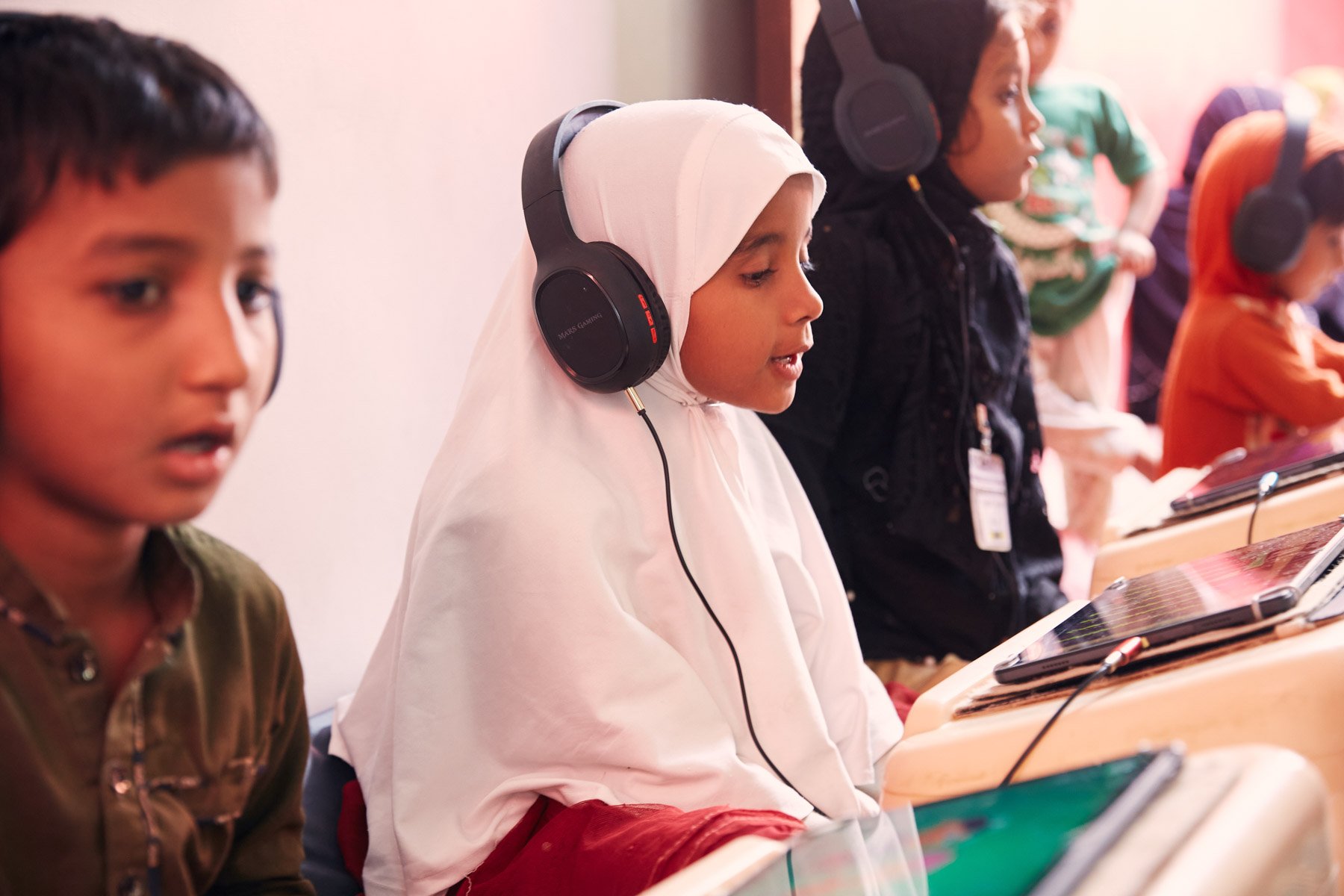 Children wearing headphones and using tablets in a classroom. For Teach the World Foundation, Razzaqabad, Karachi, Pakistan.