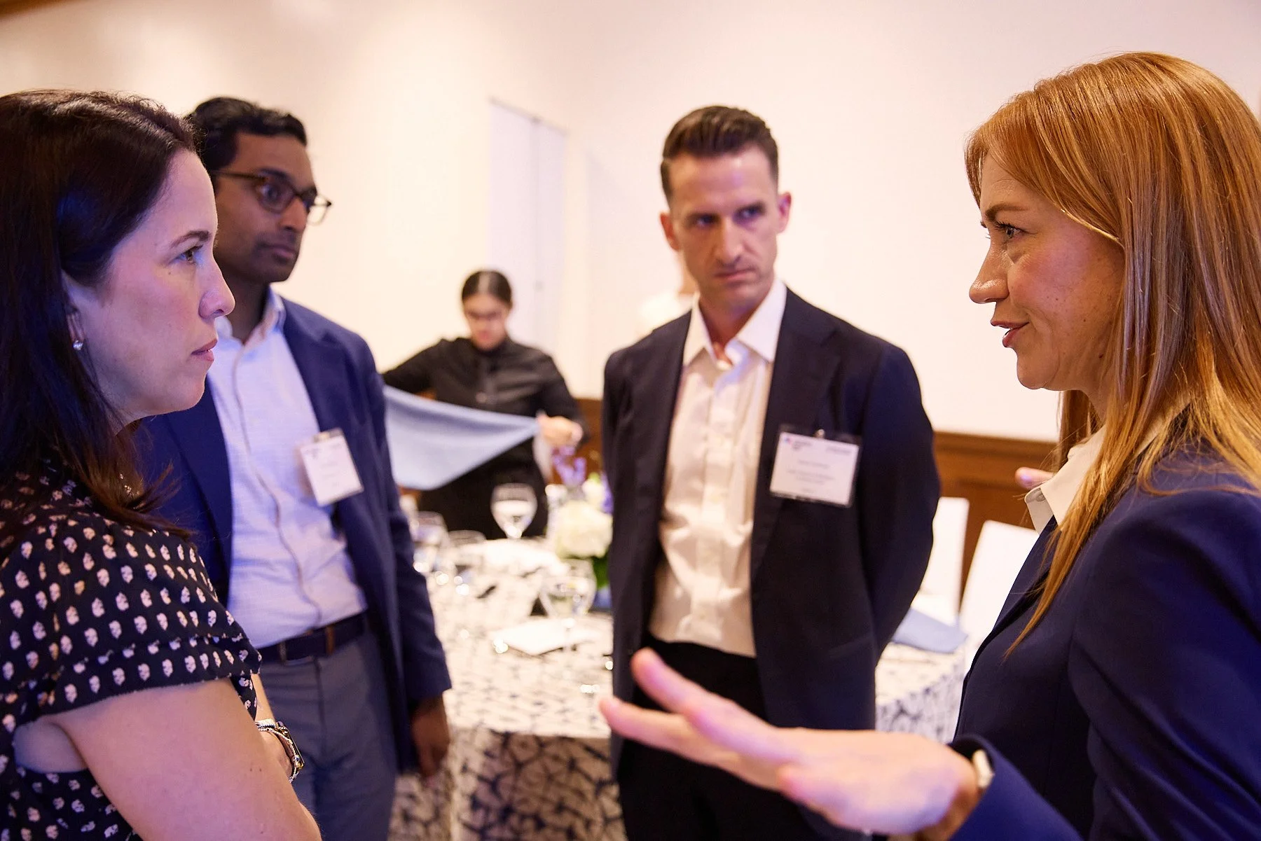 Four people engaged in conversation at a professional event or meeting in a room with a table set for a meal.