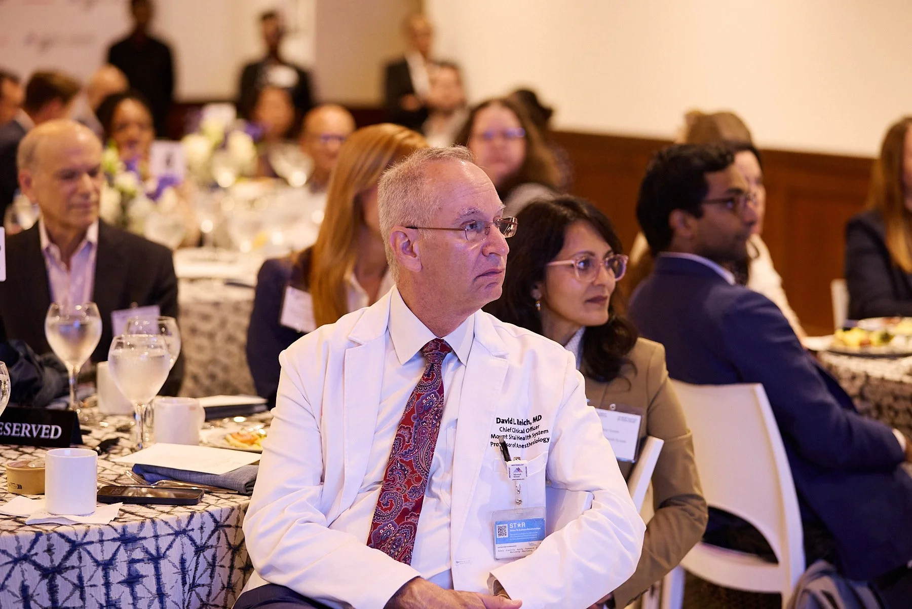 Medical professionals and conference attendees seated at tables during a presentation or seminar.