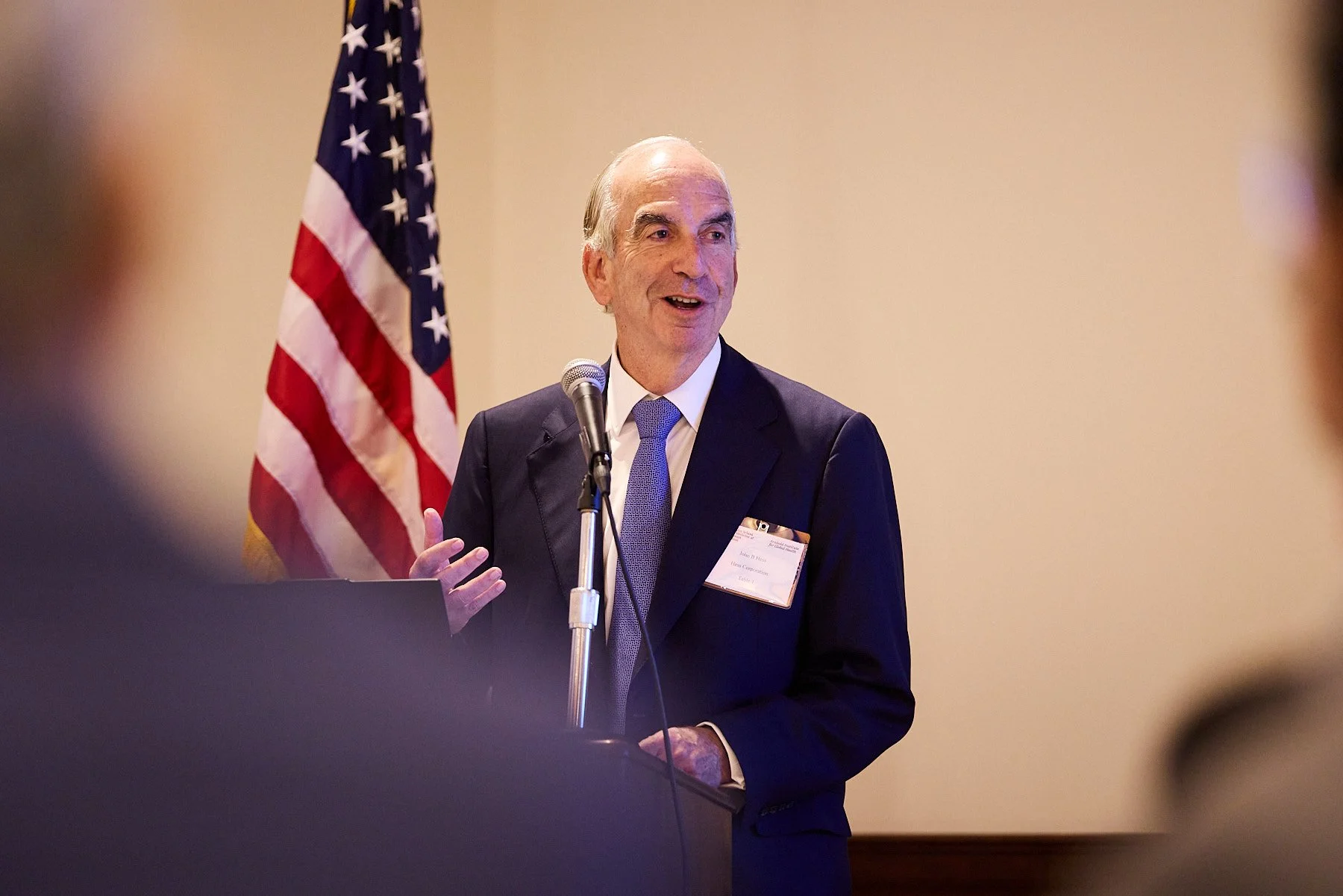 A man in a suit giving a speech at a podium with an American flag in the background.
