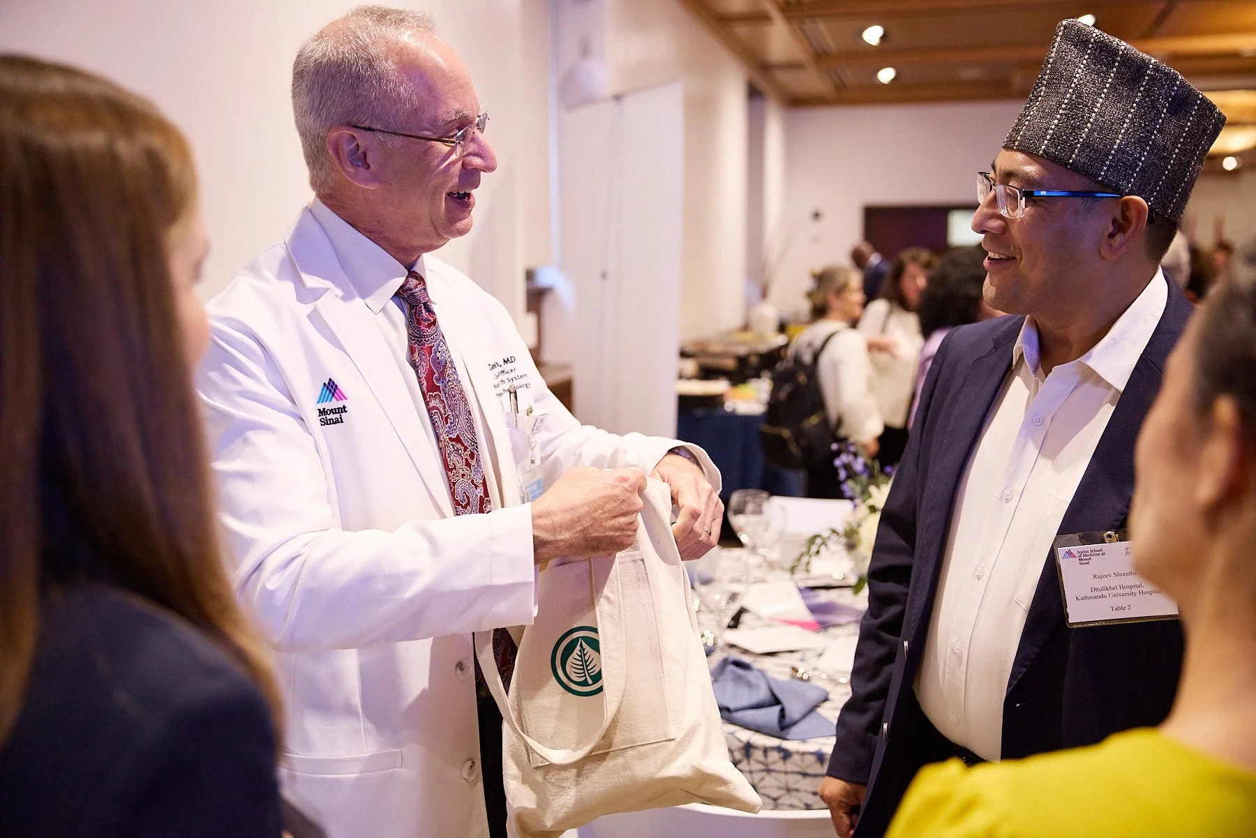 A doctor in a white coat and a man in a dark suit talking at a conference or event.