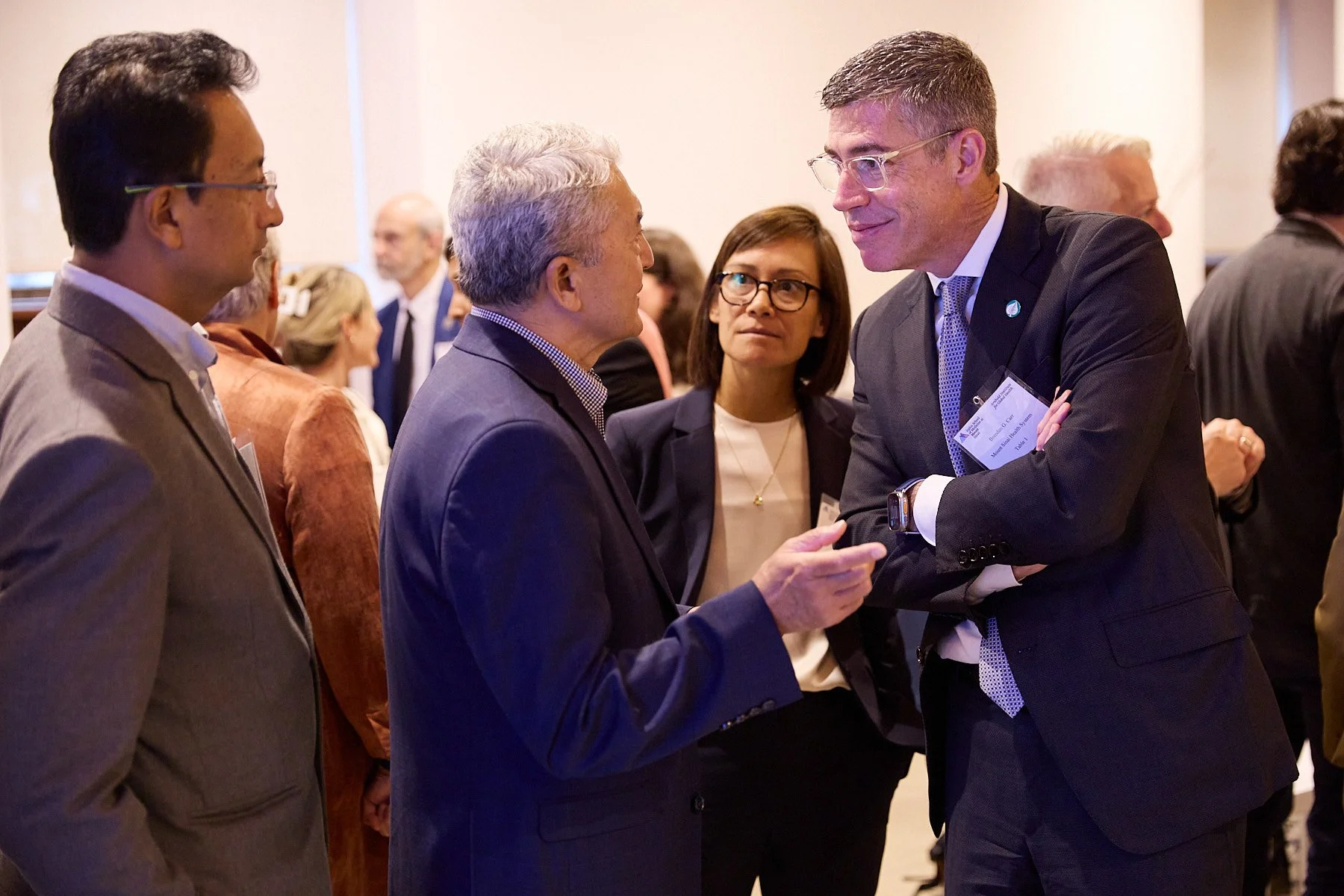 Four professionals engaged in conversation at a conference, with two men in the foreground and two women in the background.