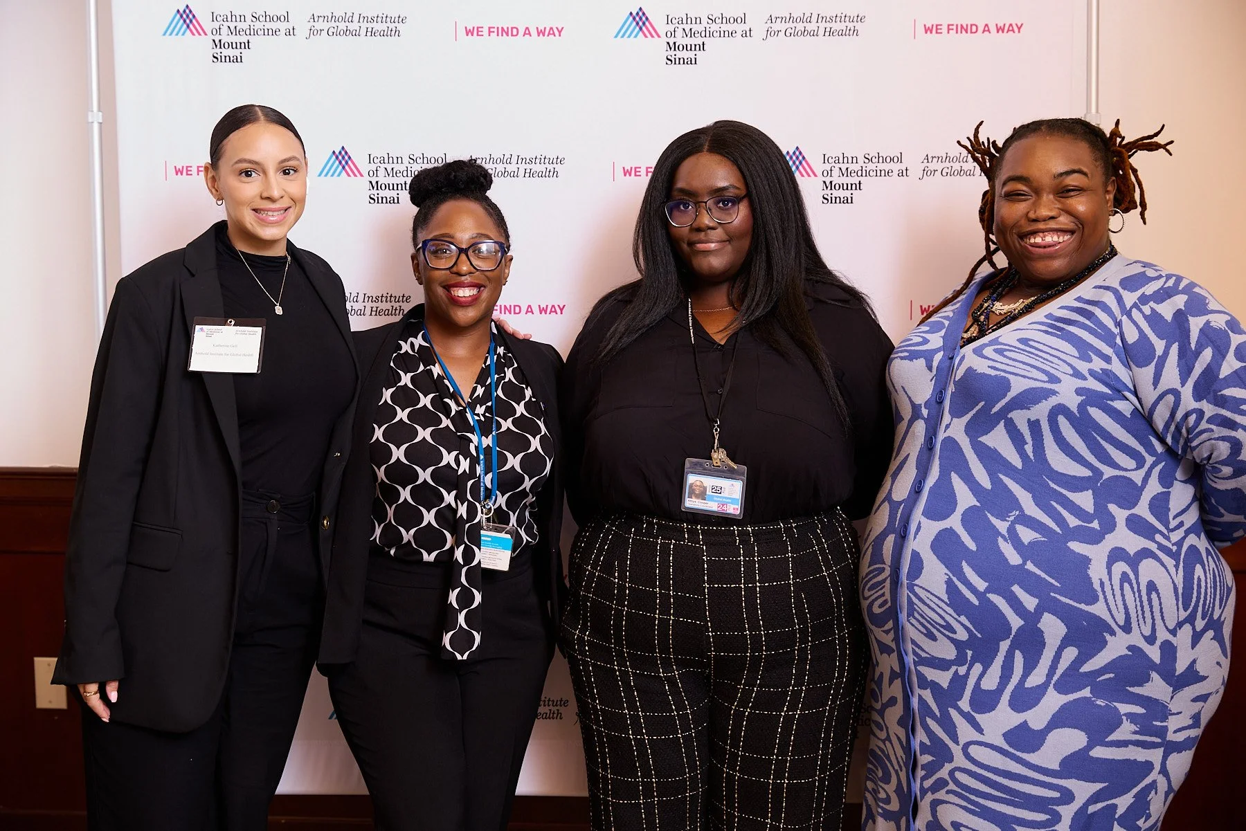Four women standing in front of a backdrop with logos and slogans, smiling for a photo at an event related to the Icahn School of Medicine at Mount Sinai and the Arnold Institute for Global Health.