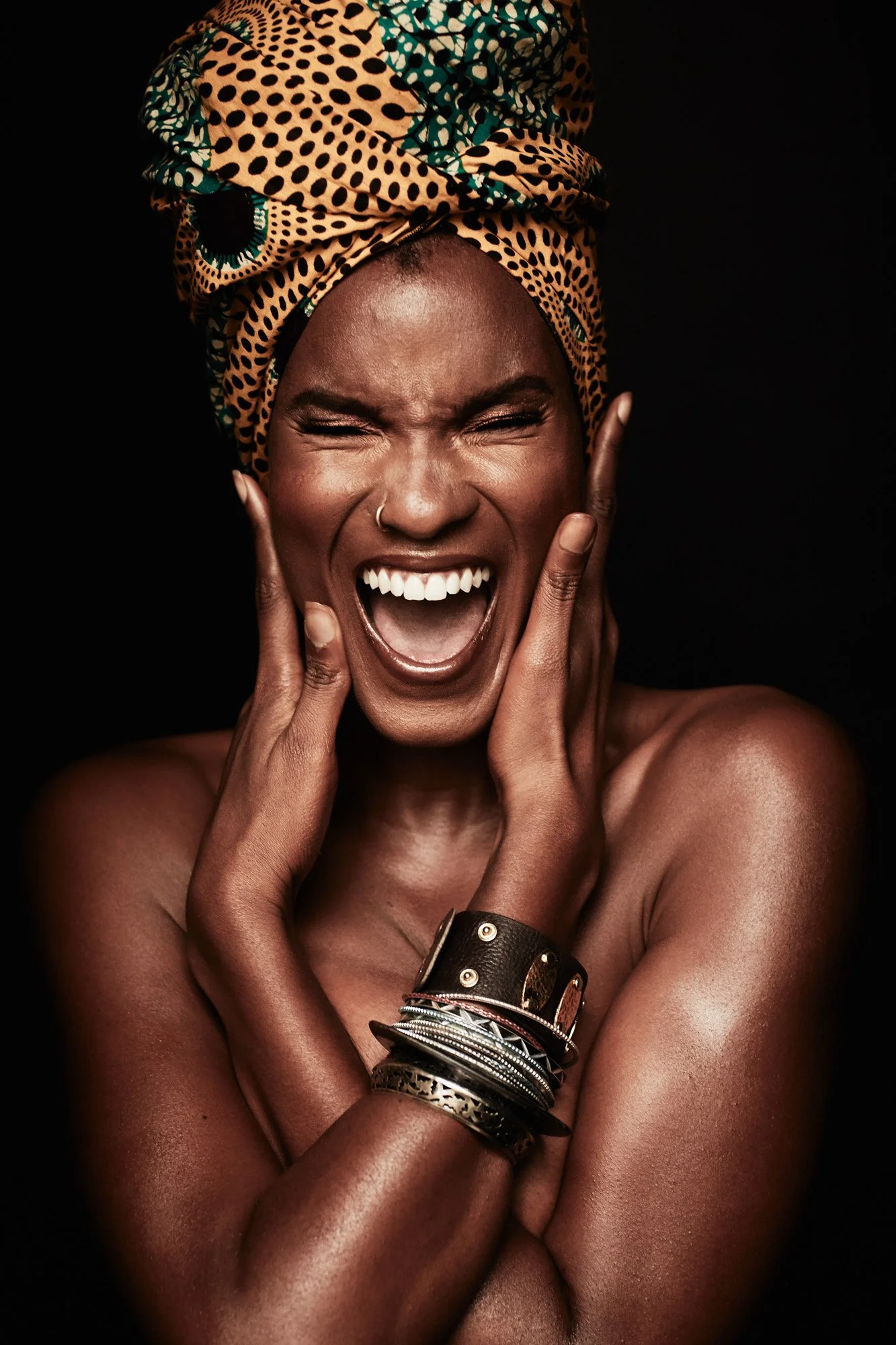 Black woman with a patterned headwrap, expressing joy with closed eyes and open mouth, wearing multiple bracelets.
