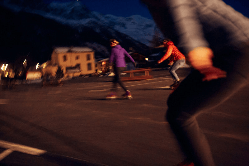 People roller skating outdoors at night with mountains and buildings in the background in Chamonix France