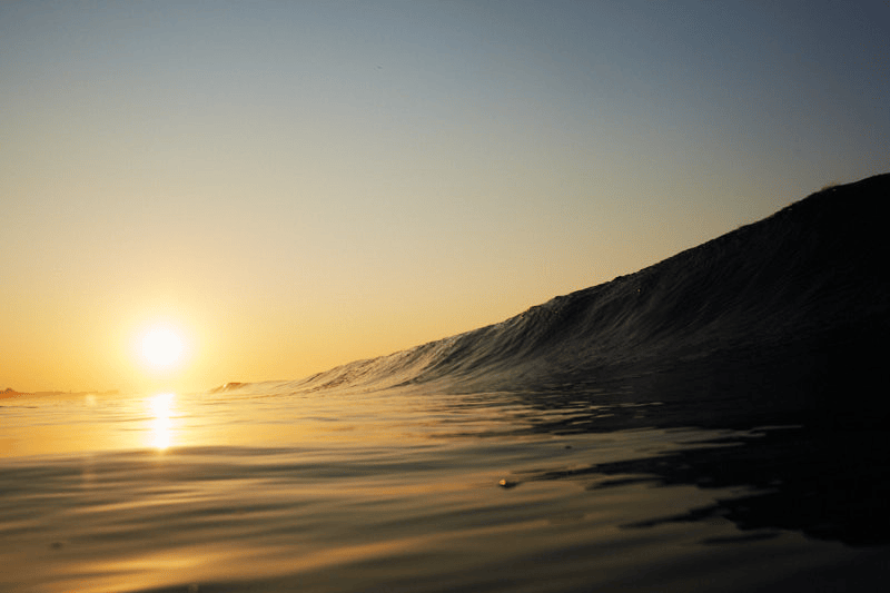 A sunrise over the ocean with a barreling wave approaching the shore, in Puerto Escondido, Oaxaca, Mexico.