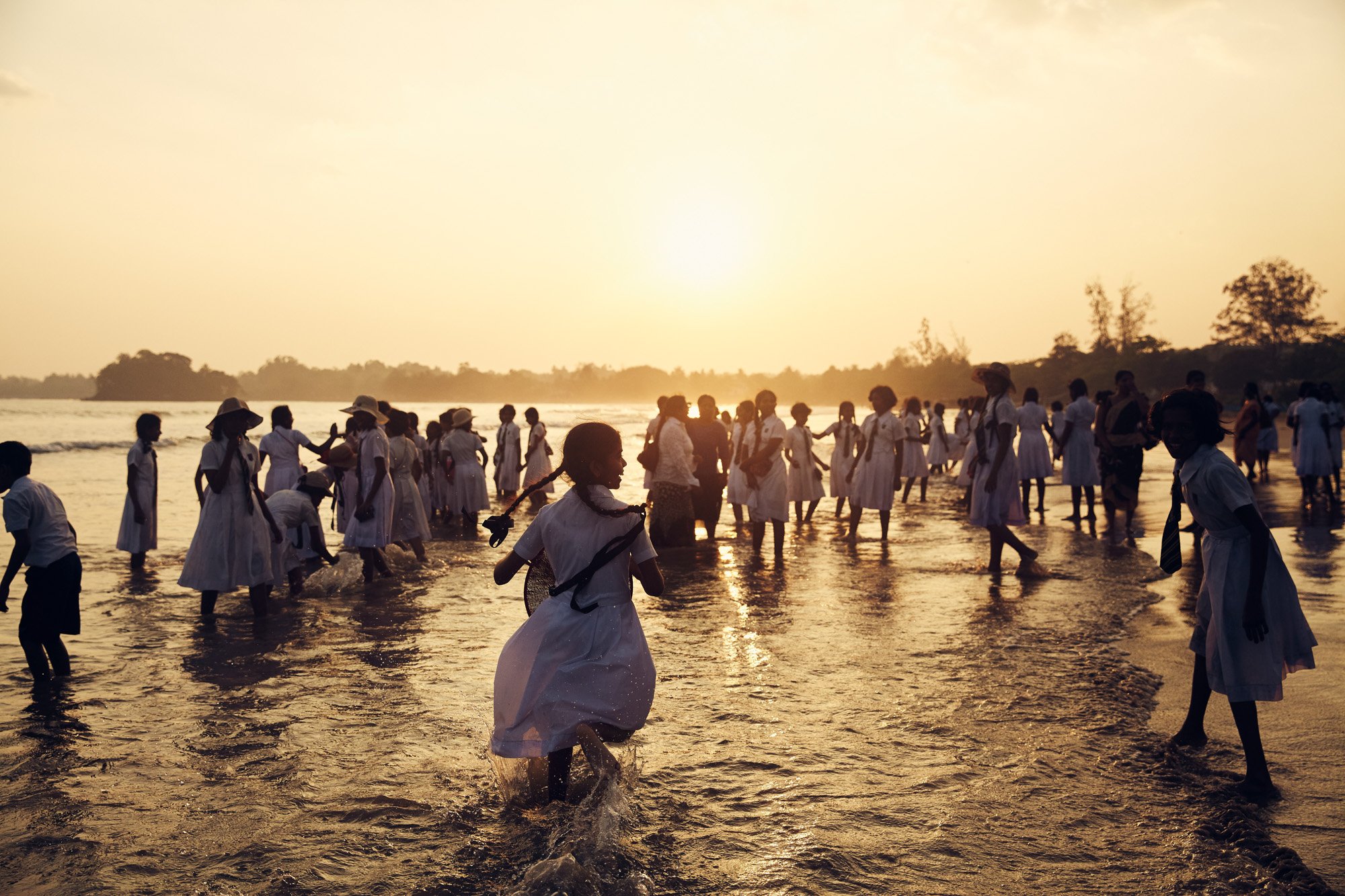 Children in school uniforms playing in the water at sunset on a beach in Weligama Sri Lanka