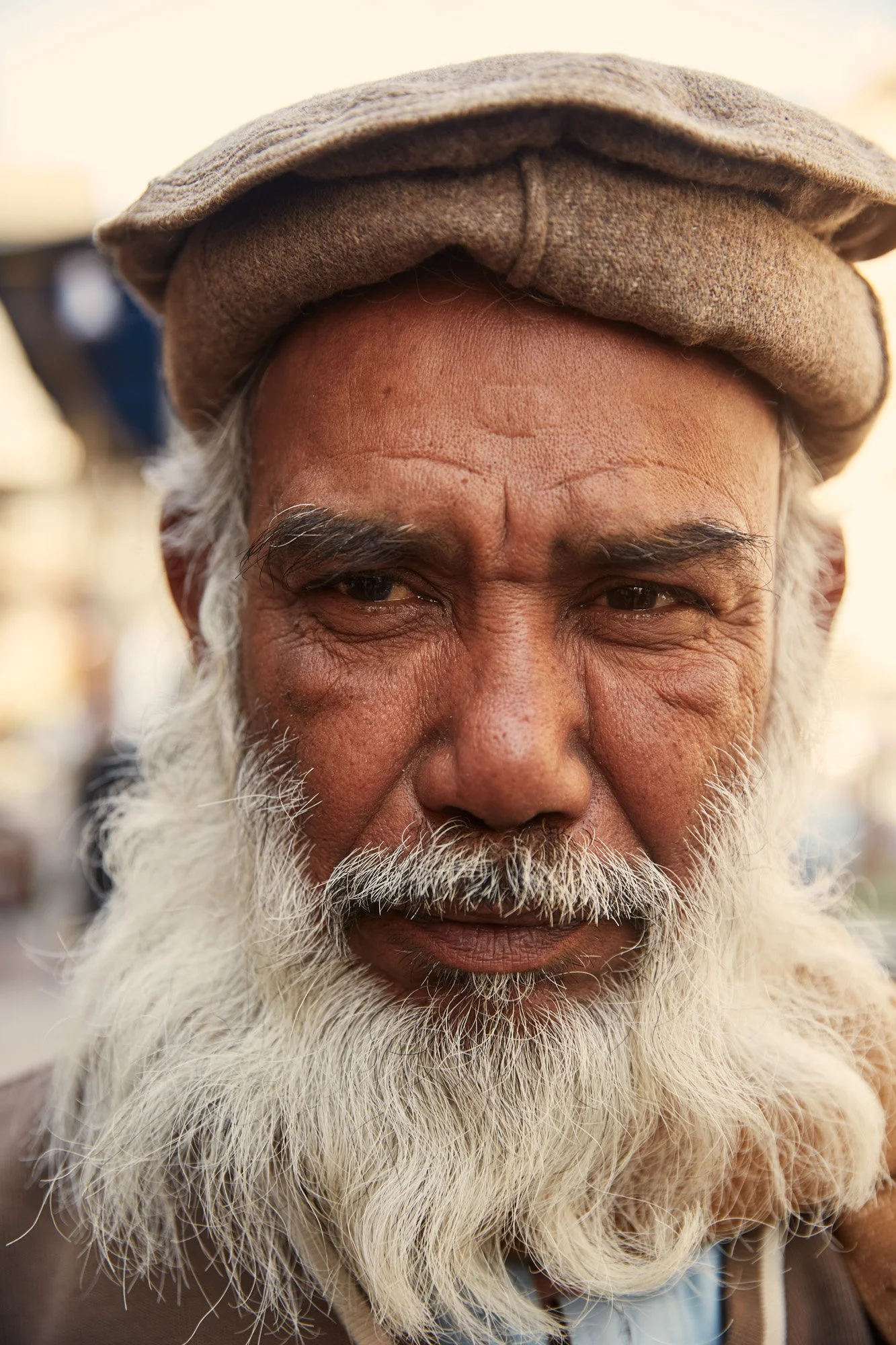 Close-up portrait of an elderly man with a long white beard wearing a gray cap, looking directly at the camera. Karachi Pakistan