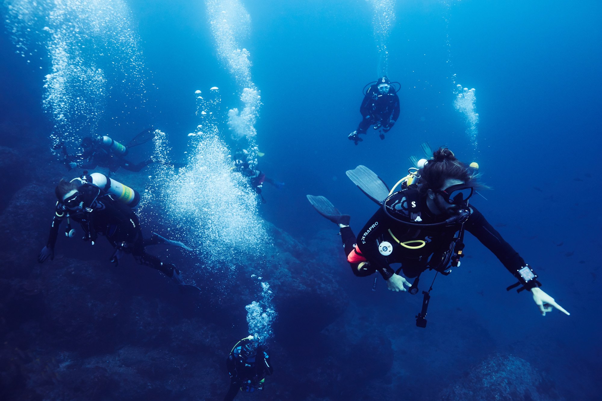 Group of scuba divers swimming underwater in clear blue ocean, exploring coral reef in Cocos Island, Costa Rica.