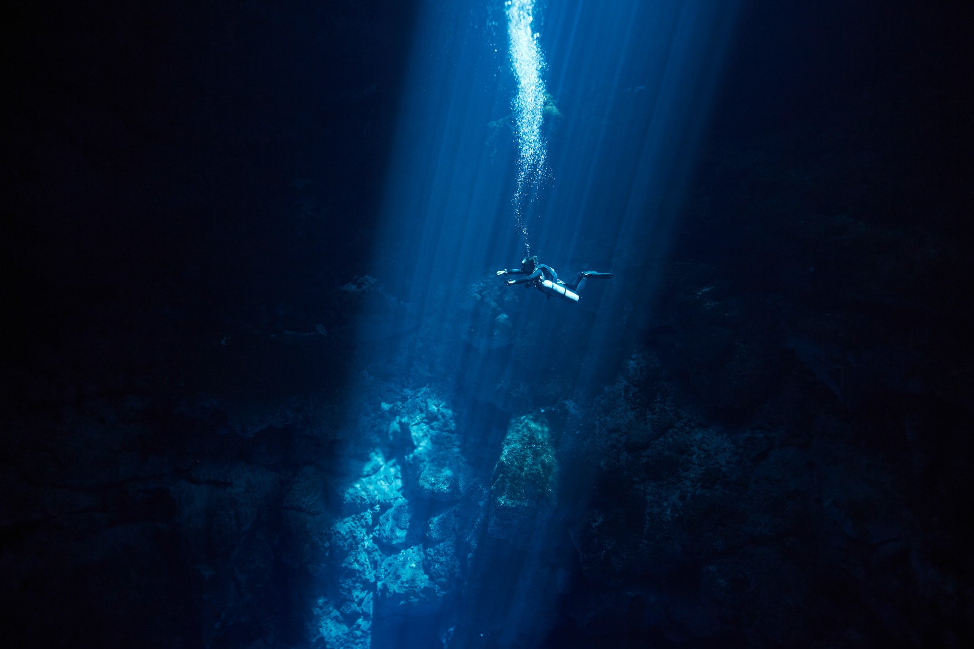 A scuba diver swimming in an underwater cave illuminated by a shaft of light, El Pit, Yucatan, Mexico.