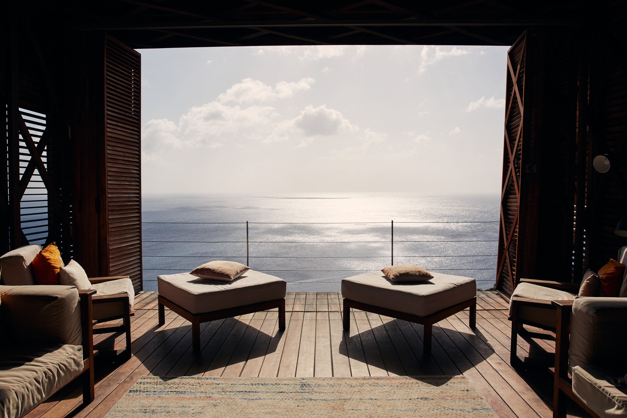 Balcony seating with cushioned chairs and ottomans overlooking the ocean under a cloudy sky in St Lucia.