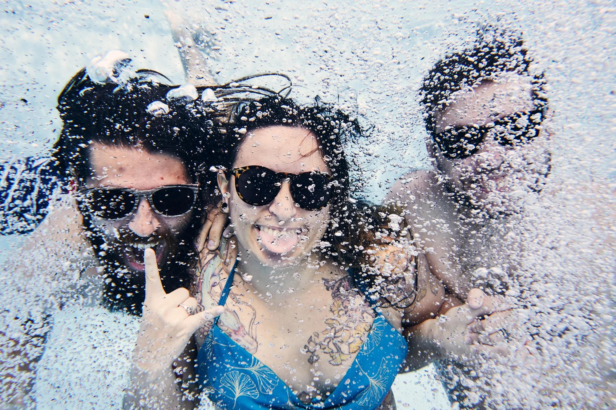 Three people underwater, wearing sunglasses and smiling